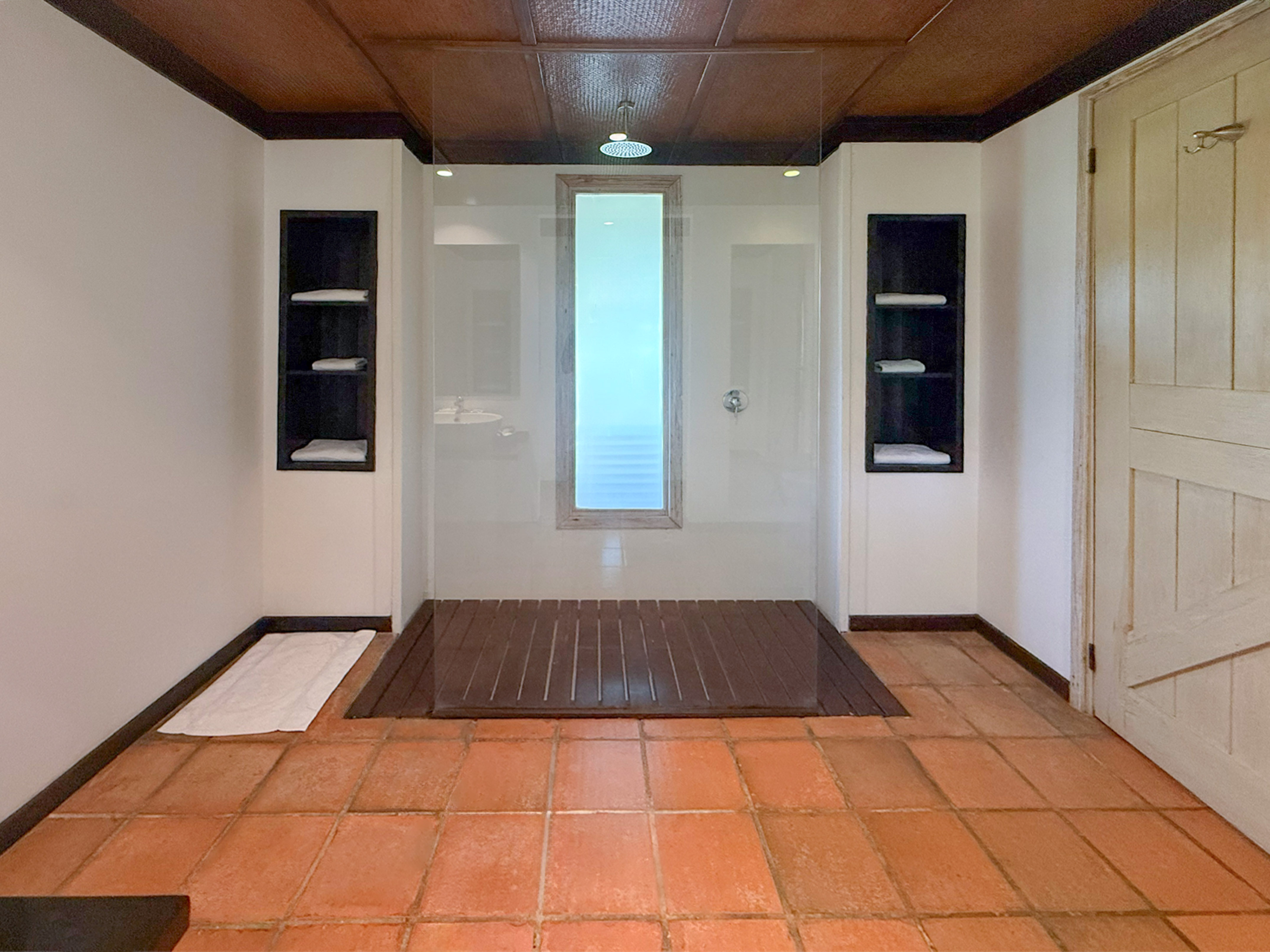 Modern walk-in shower with glass enclosure, rain head, wood floor, terracotta tiles.