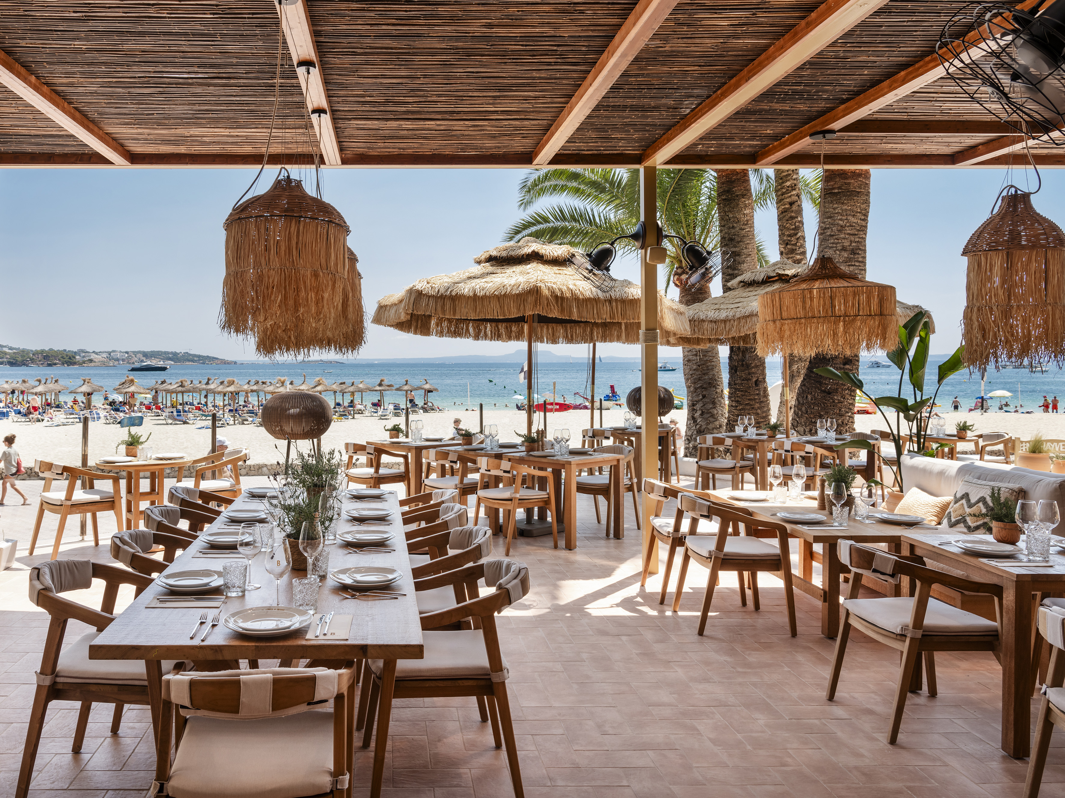 Beach club dining area with ocean view, wooden furniture, and straw decor.