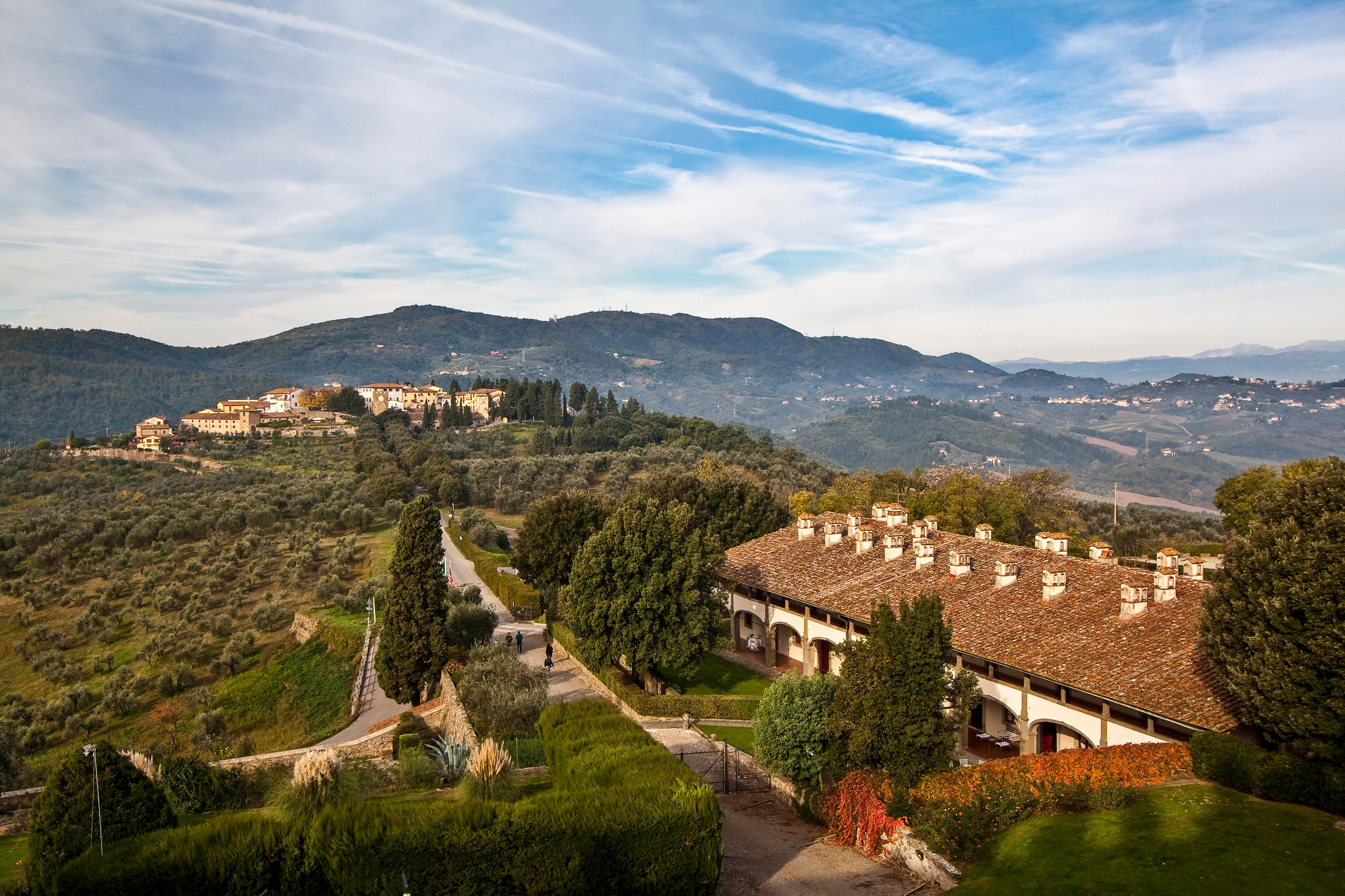 Tuscan hills, olive groves, historic village, and traditional Italian villa.