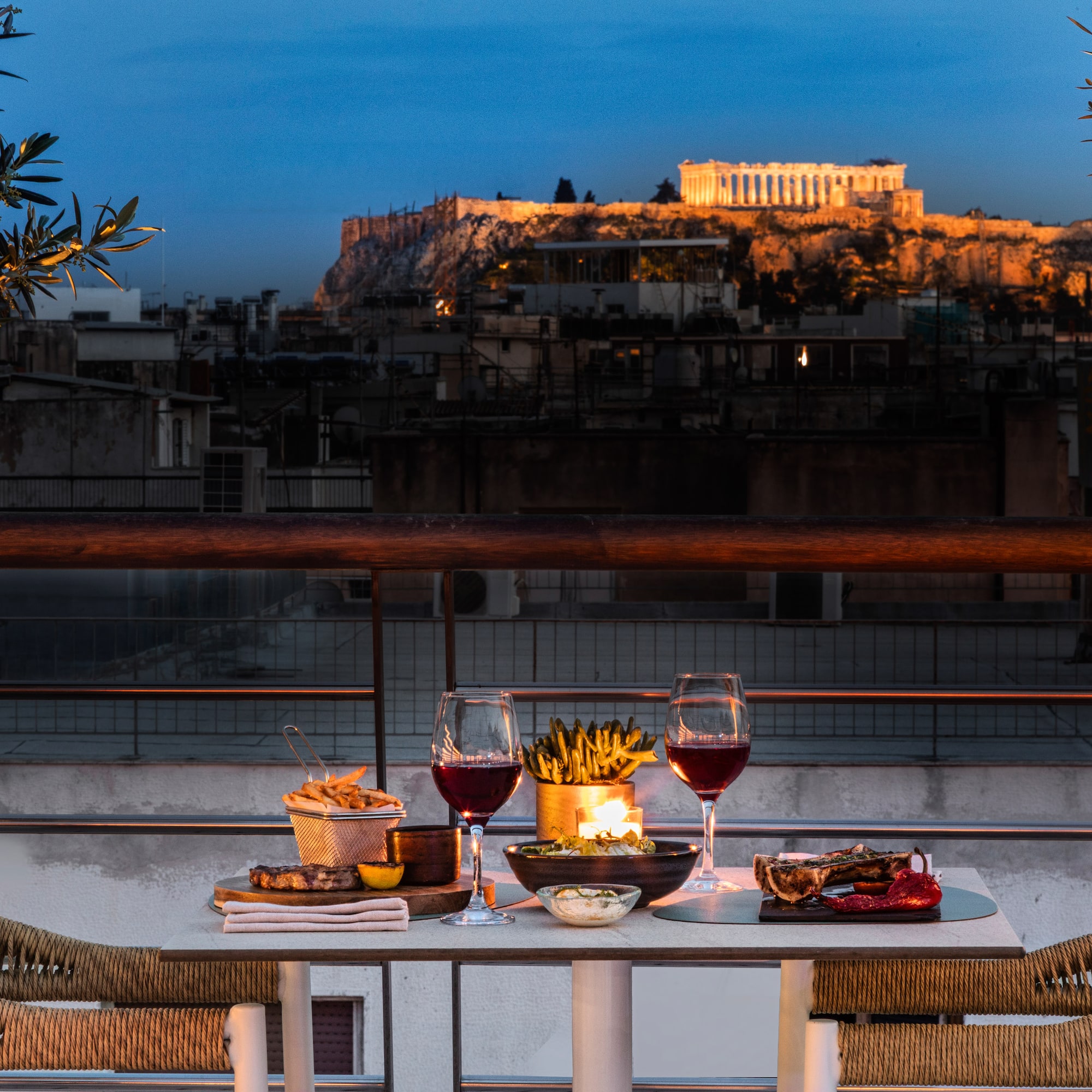 Rooftop dinner overlooking the illuminated Parthenon in Athens at dusk.