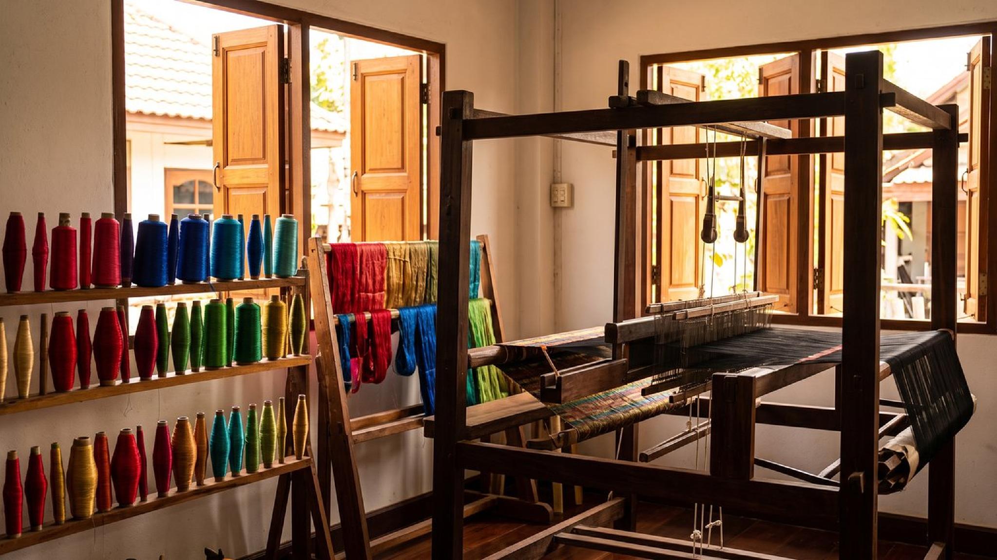 Wooden weaving loom with shelves of colorful yarn spools in a sunlit craft room.