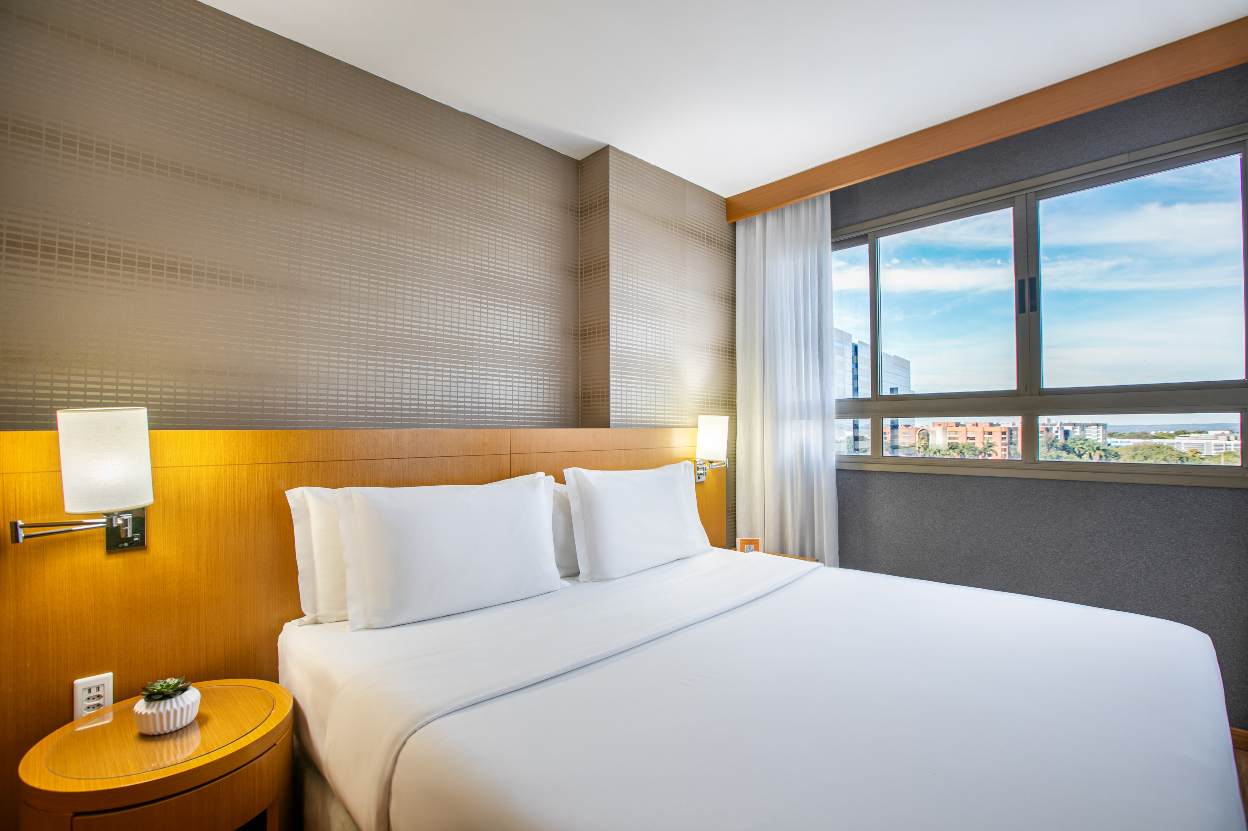 Bright modern hotel room with white bed, wooden headboard, and city view.