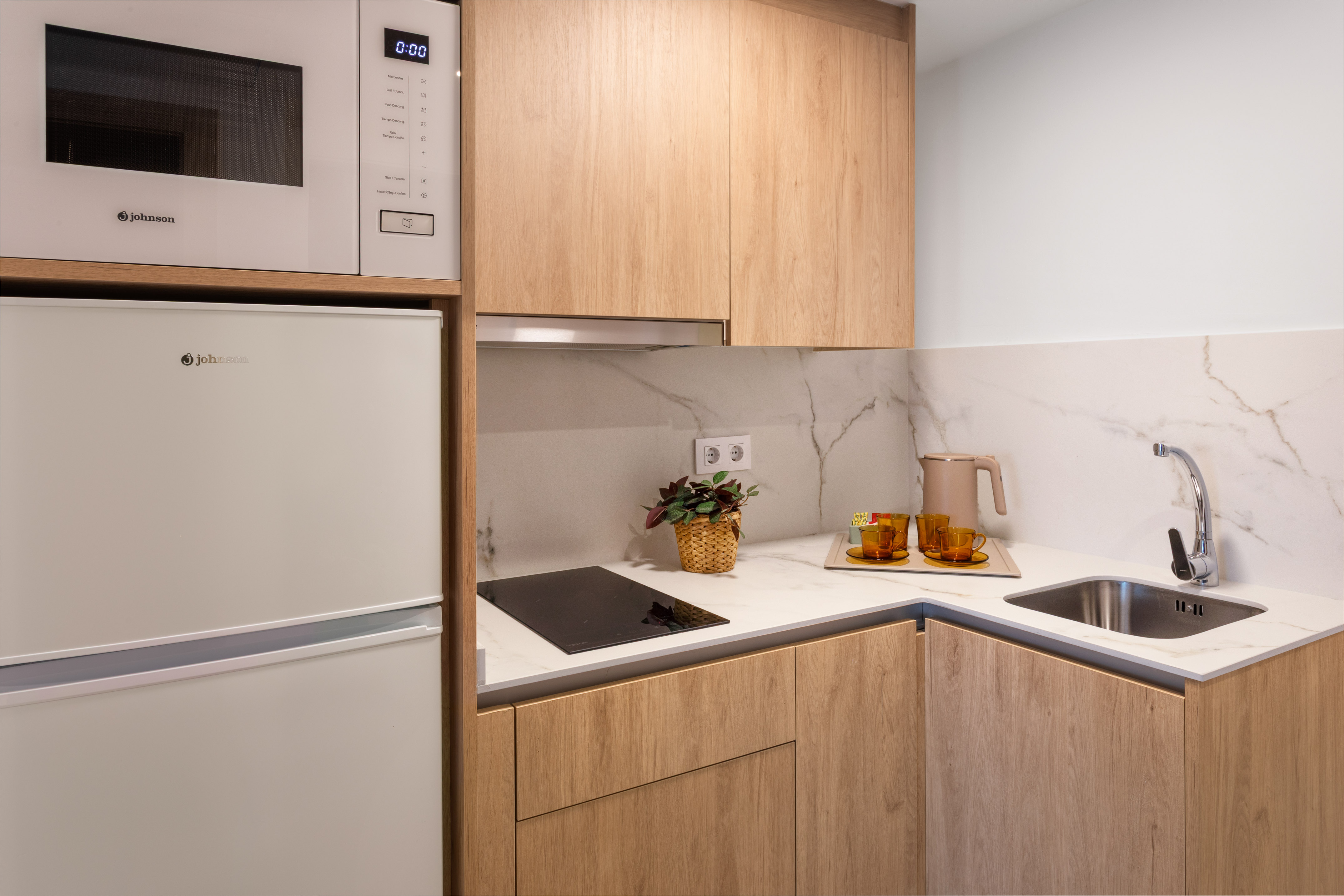 Compact modern kitchen with wood cabinets, white appliances, cooktop, and sink.