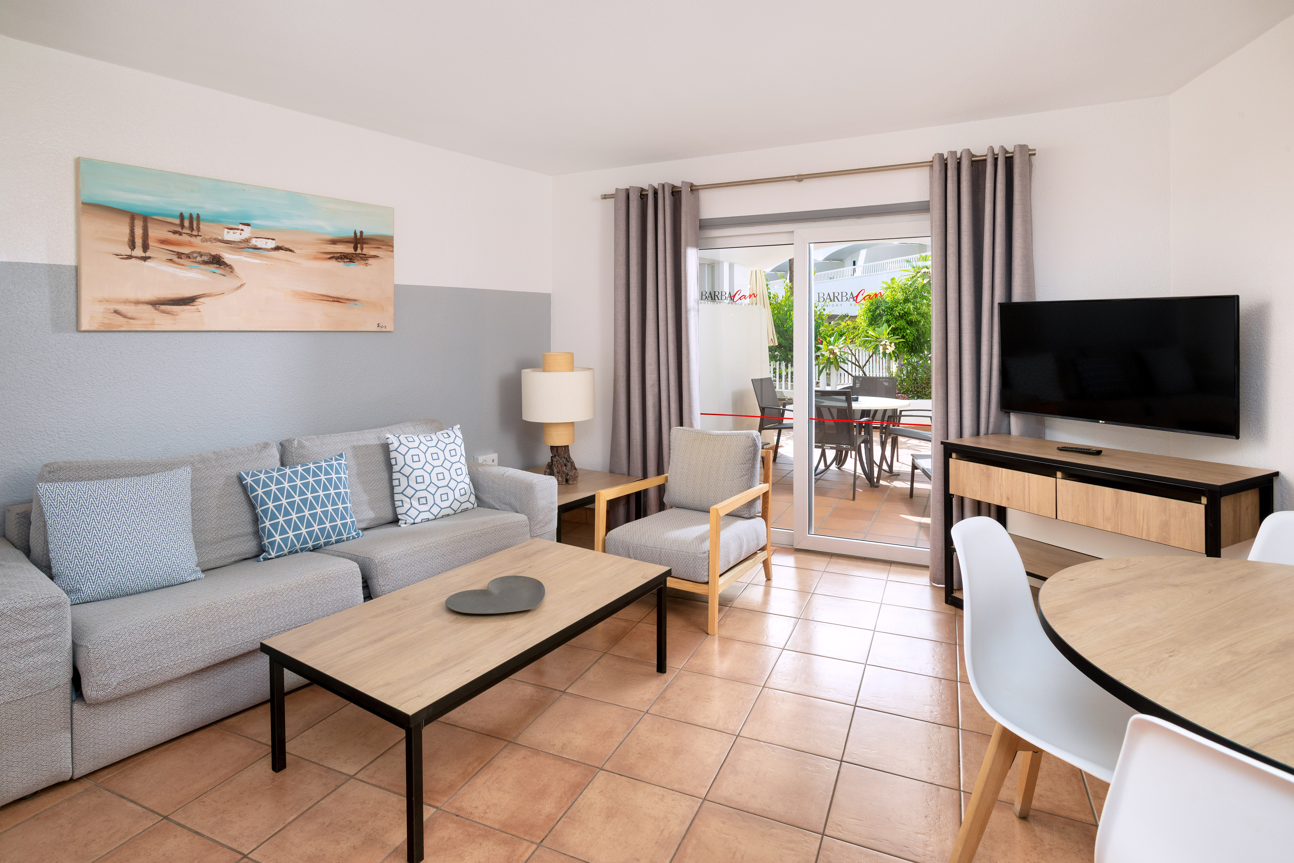 Bright apartment living room with grey sofa, dining set, TV, and patio access.