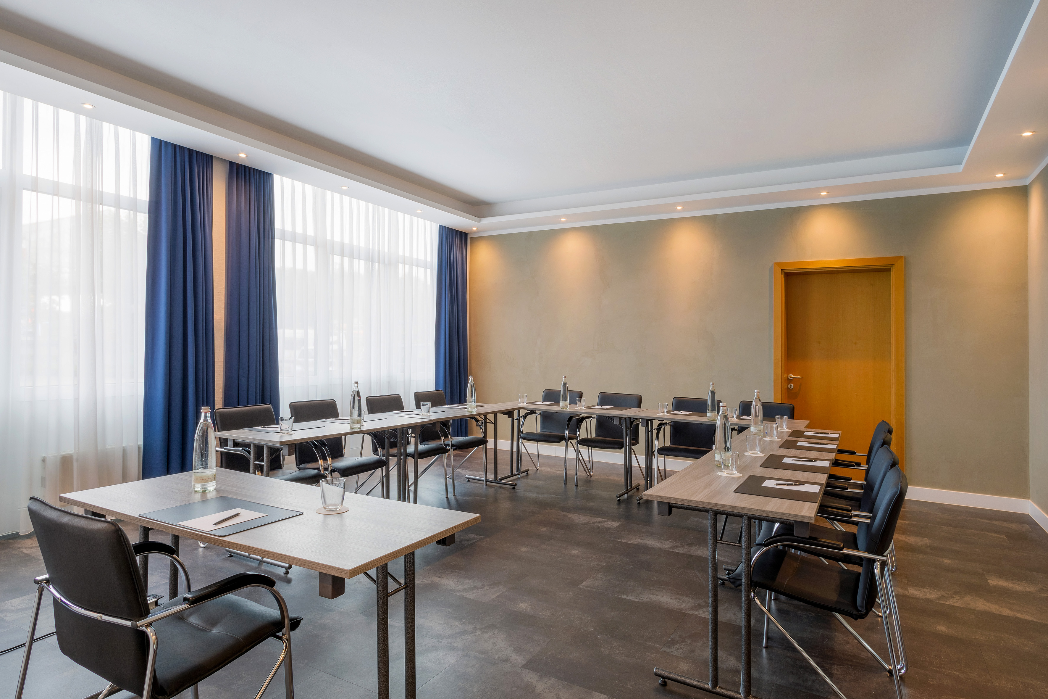Modern conference room with U-shaped tables, black chairs, and large windows.