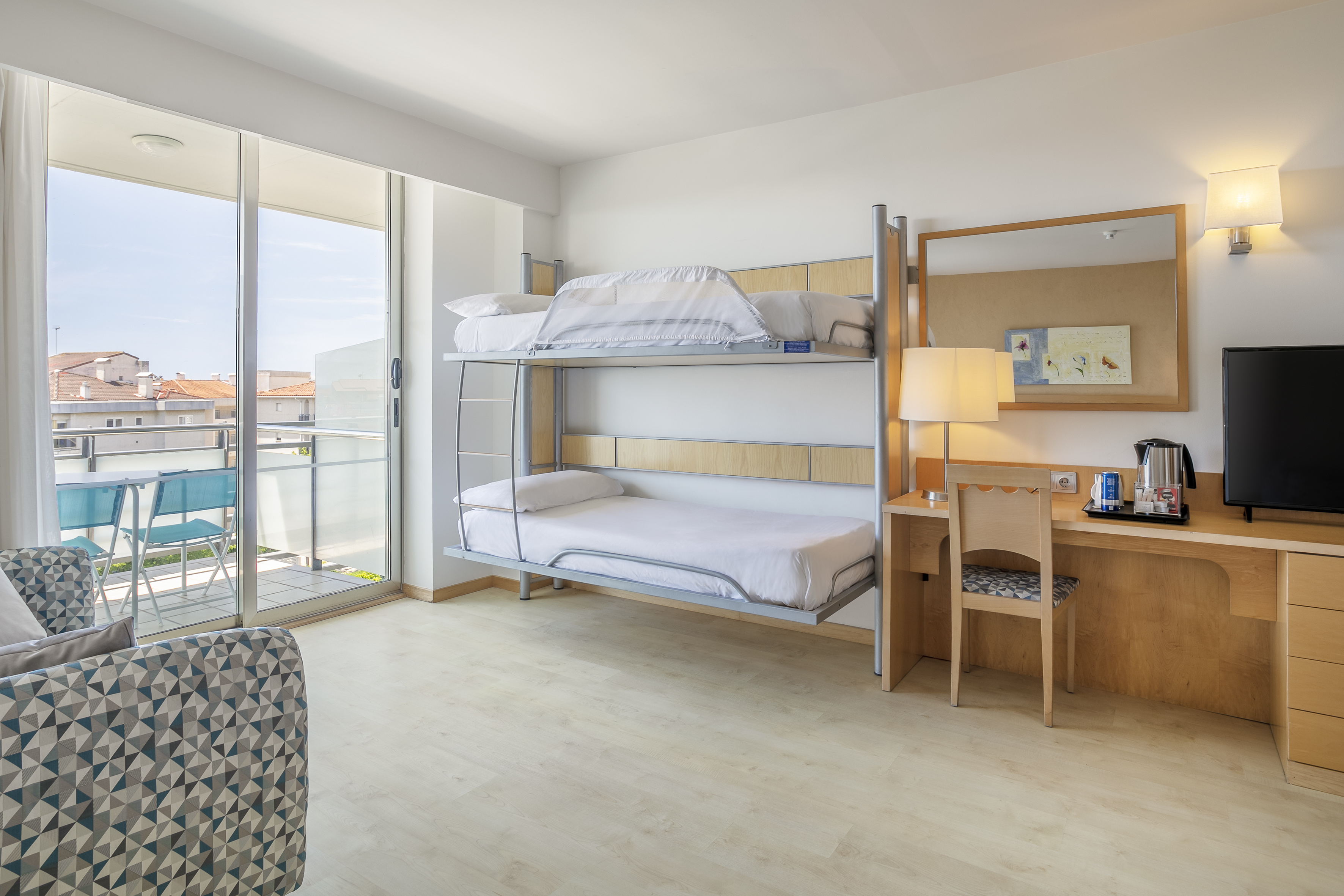 Bright family hotel room with bunk beds, work desk, and balcony city view.