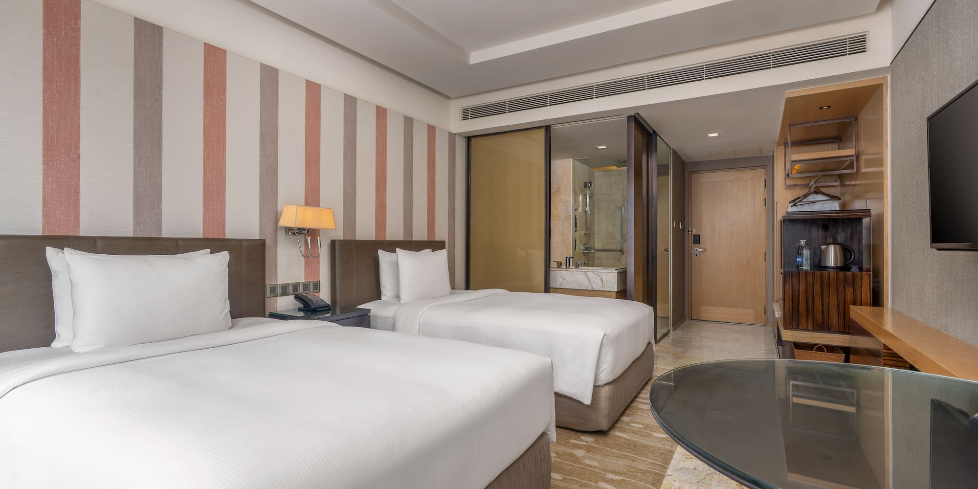 Modern hotel twin bedroom with white linens, striped accent wall, and glass desk. - Guest Room - The Hotel Bangkok Sukhumvit 26 Affiliated by Meliá, Bangkok
