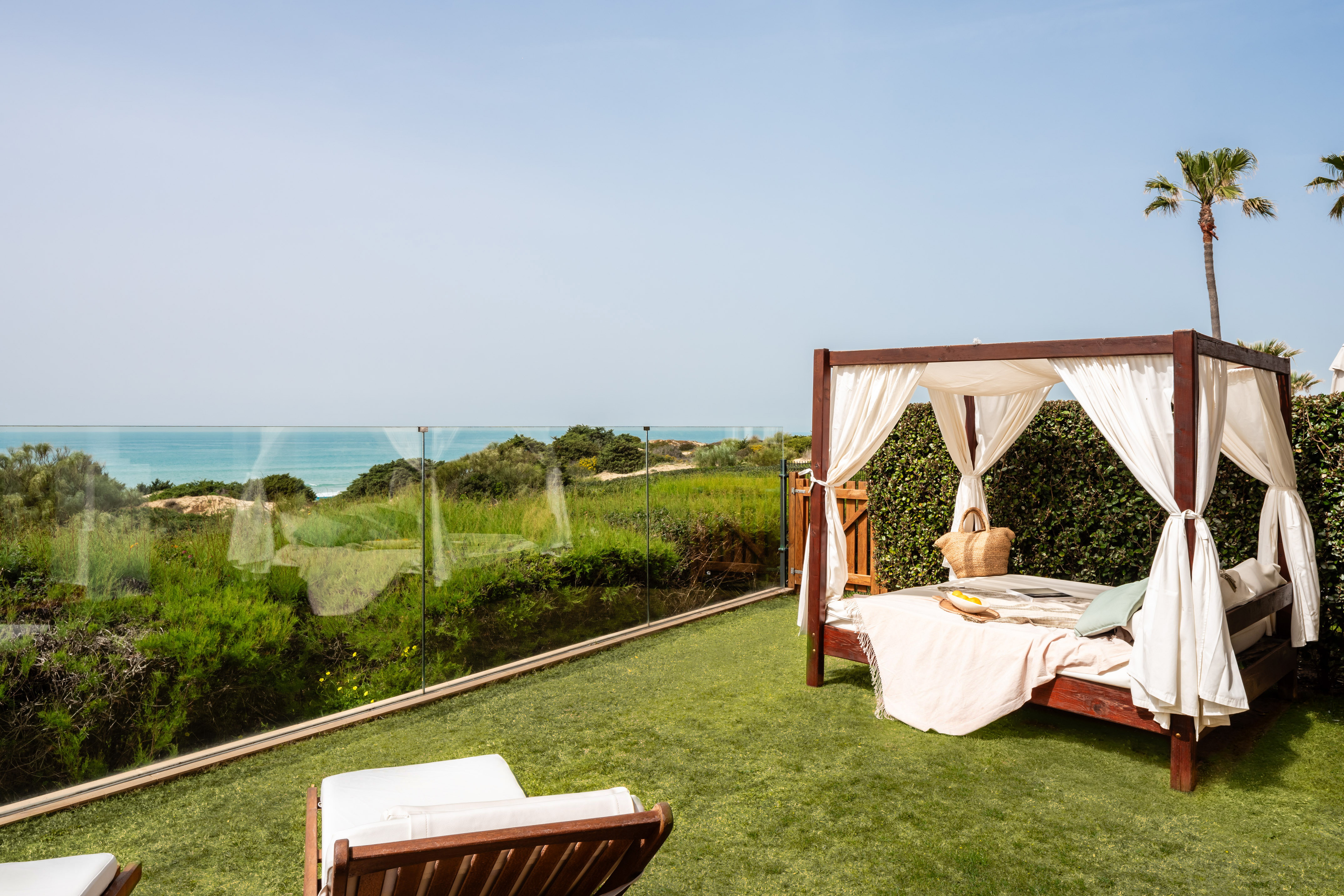 Outdoor canopy bed on green lawn with ocean view and palm trees.