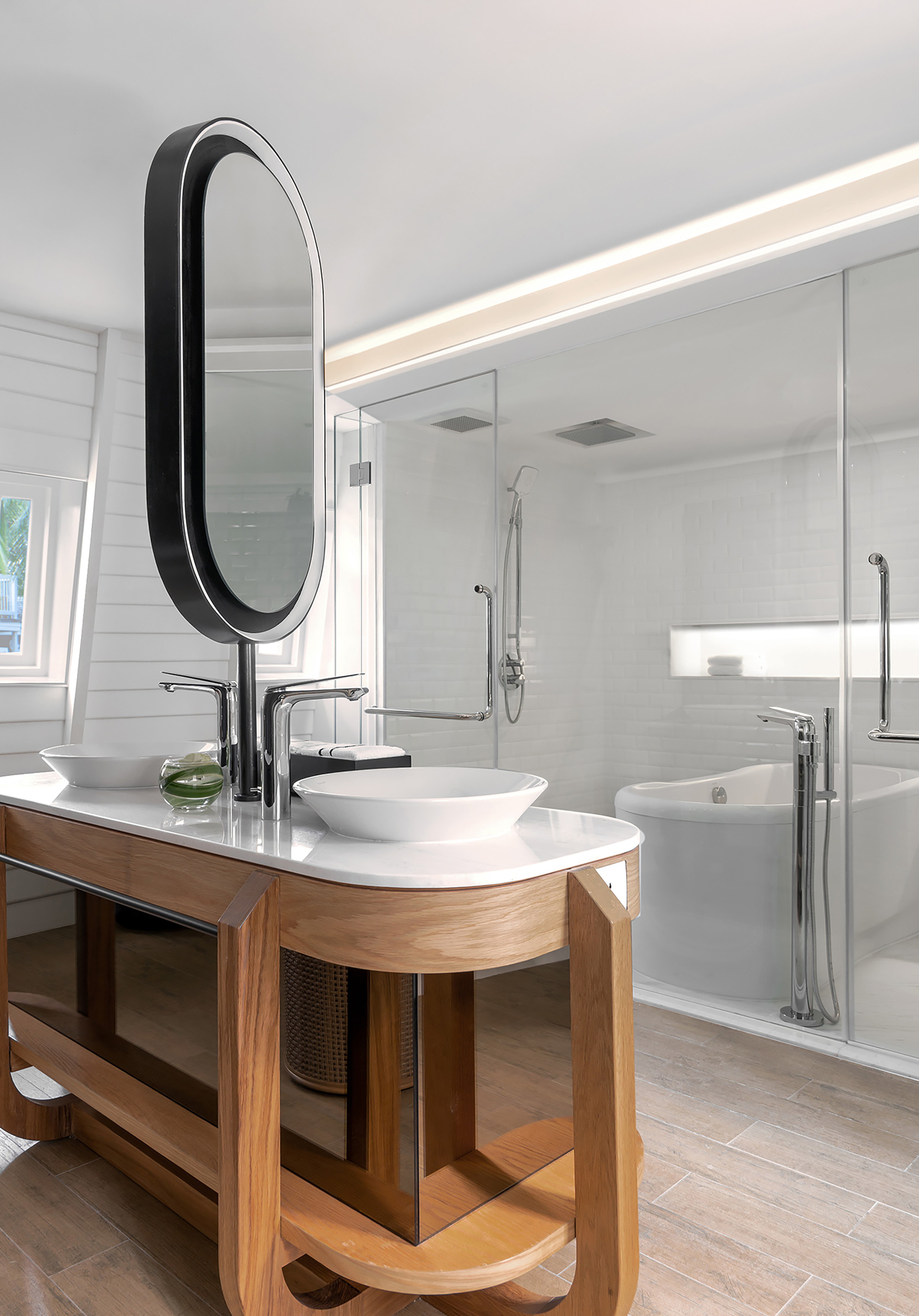 Modern bathroom with double vanity, oval mirror, glass shower, and bathtub.