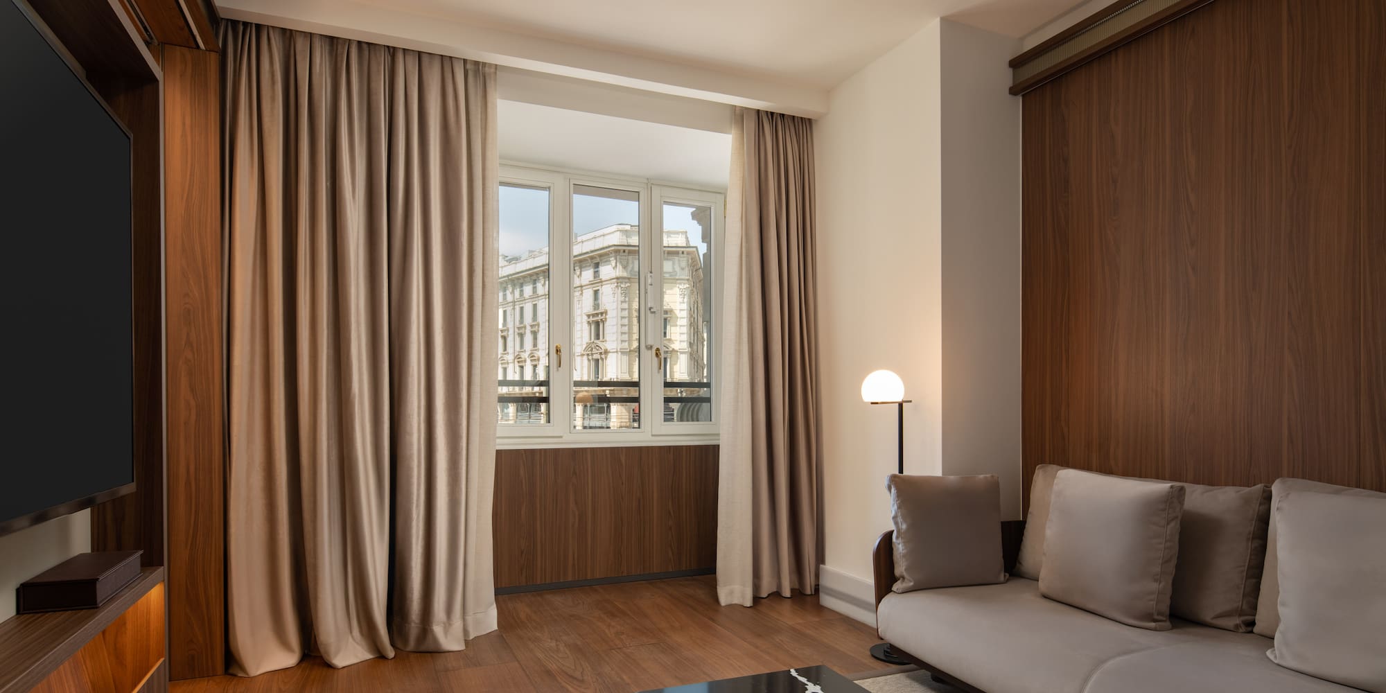 Modern hotel living room, sofa, dark wood, city view window.