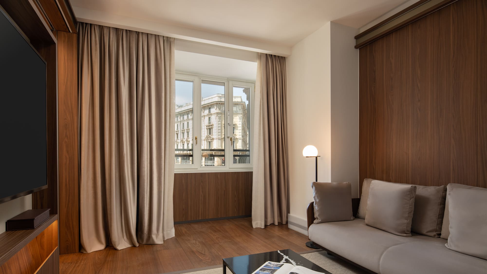 Modern hotel living room, sofa, dark wood, city view window.