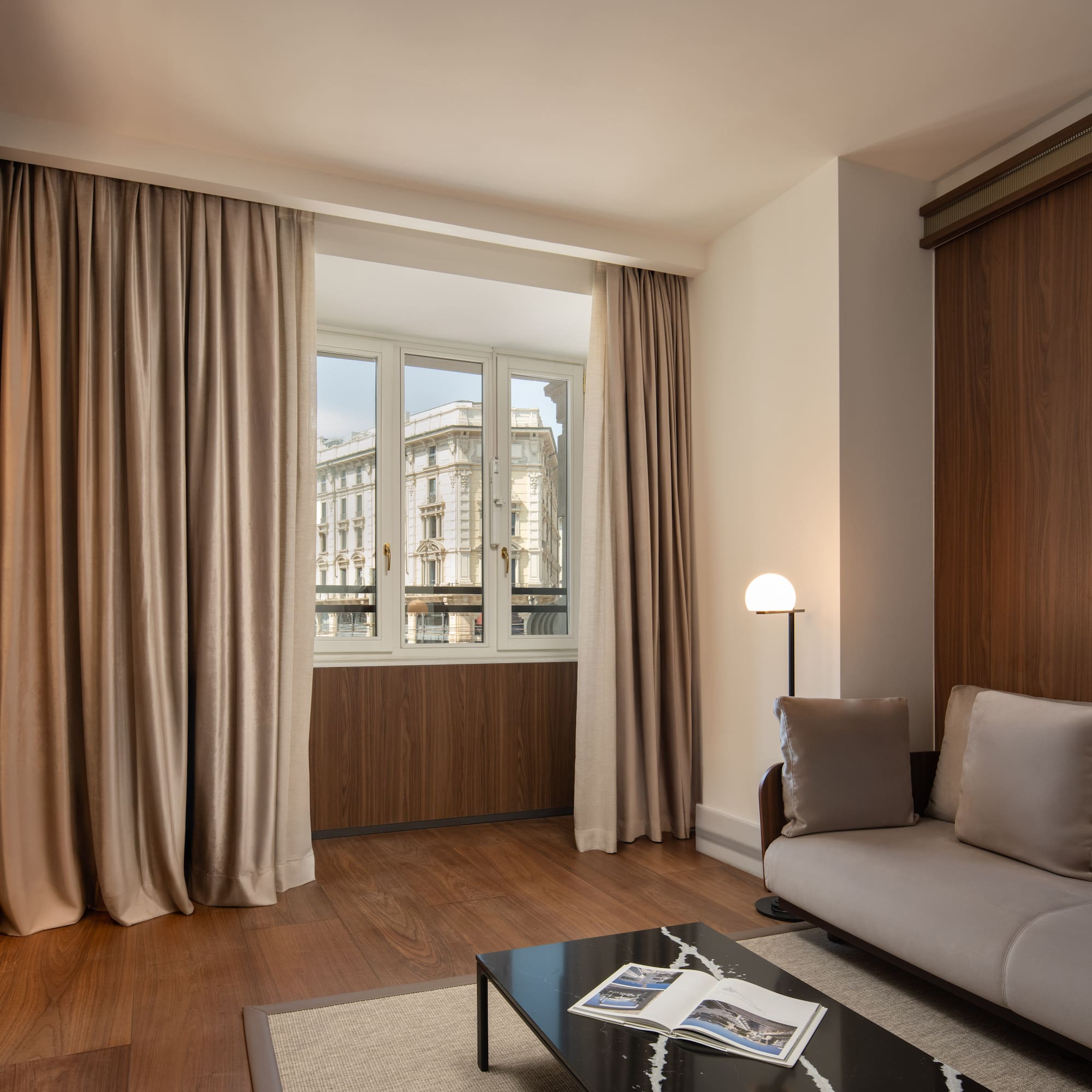 Modern hotel living room, sofa, dark wood, city view window.