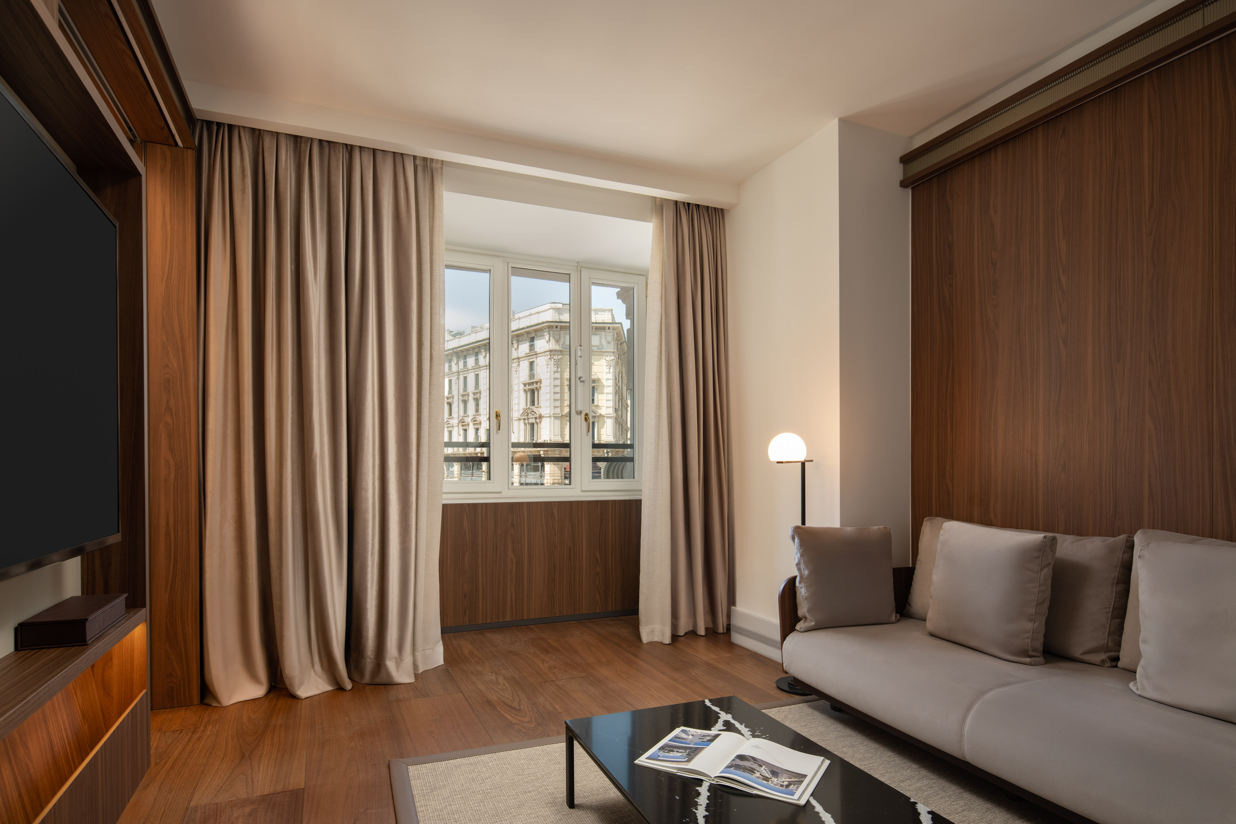 Modern hotel living room, sofa, dark wood, city view window.