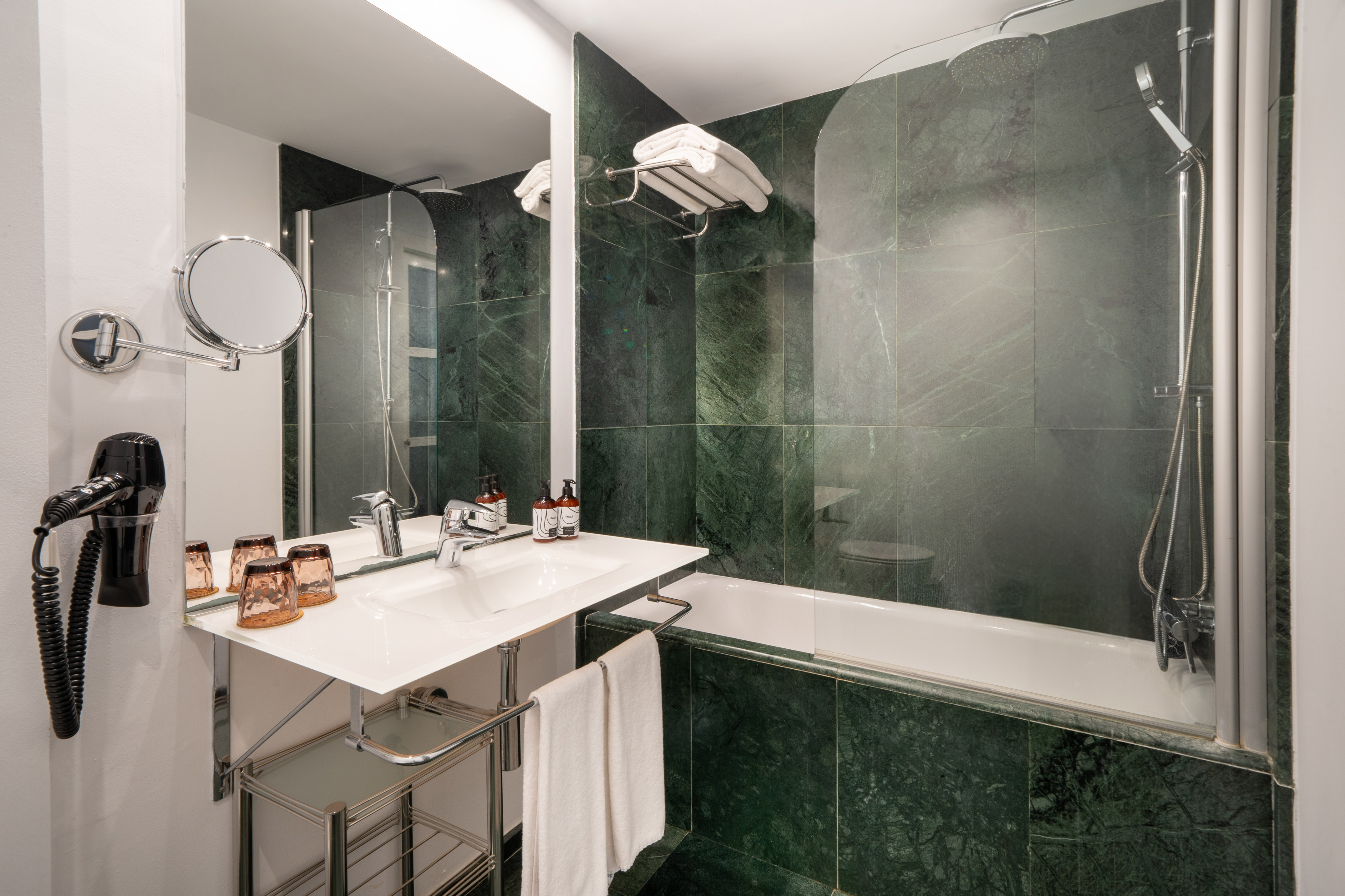 Modern hotel bathroom with green marble tiles, bathtub, sink, and mirror.