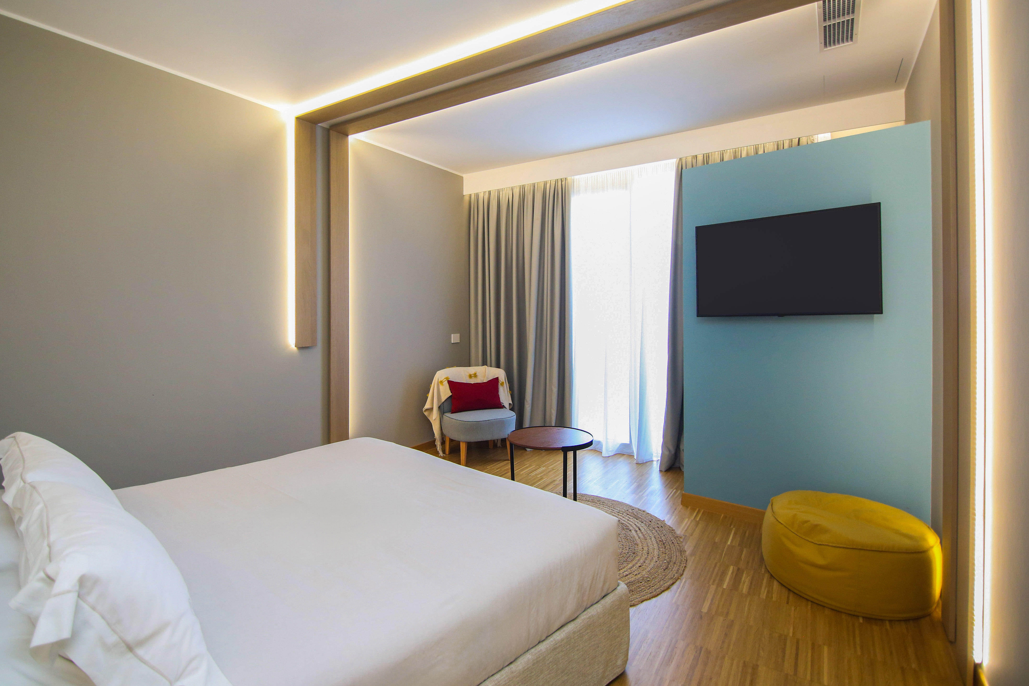 Stylish hotel room with king bed, smart TV, modern lighting, and wood floor.