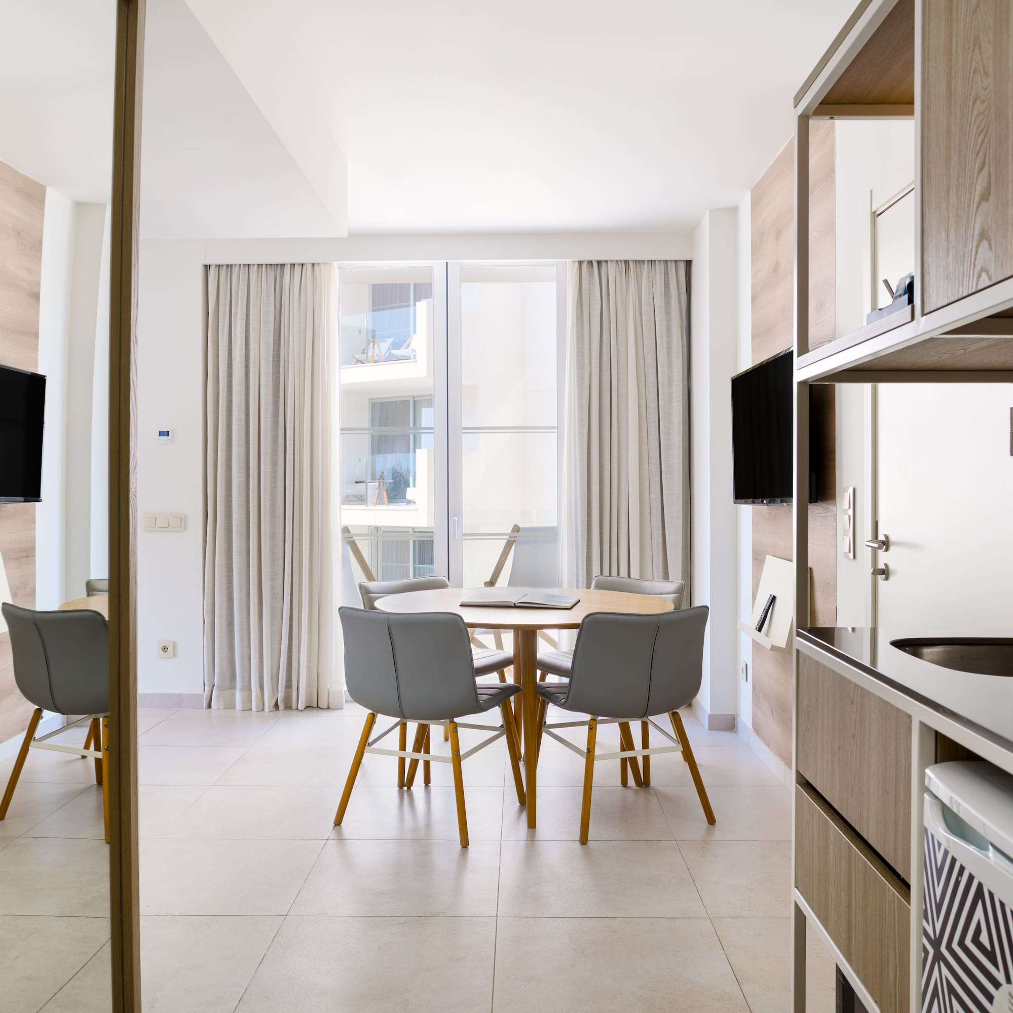 Modern hotel apartment with dining table, TV, and compact kitchenette.
