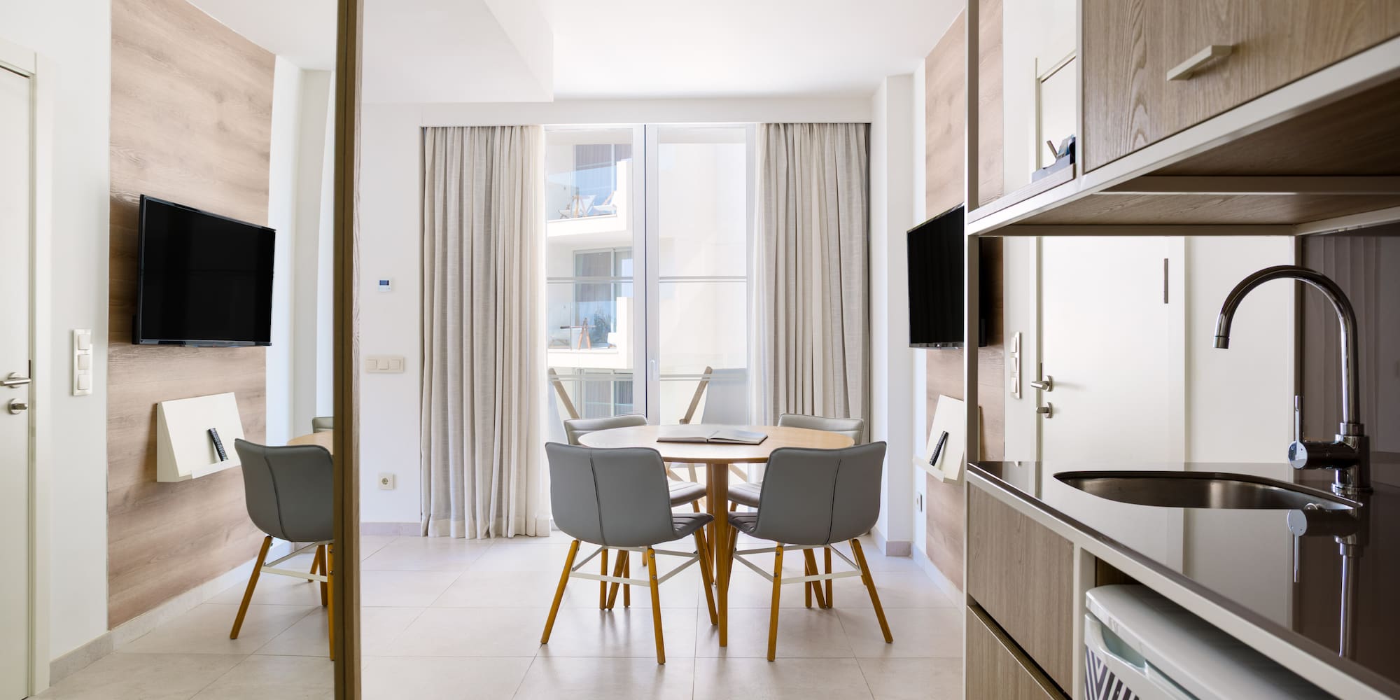 Modern hotel apartment with dining table, TV, and compact kitchenette.