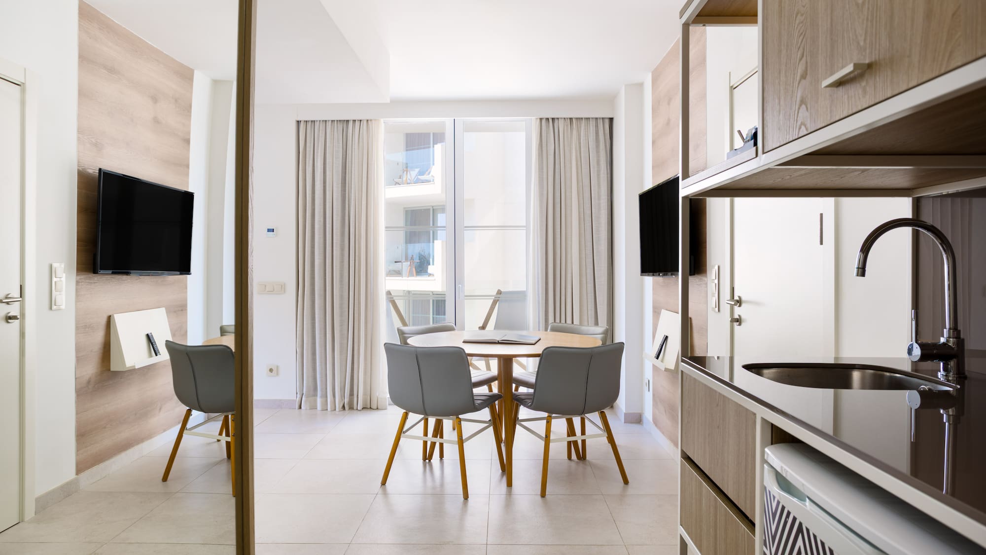Modern hotel apartment with dining table, TV, and compact kitchenette.