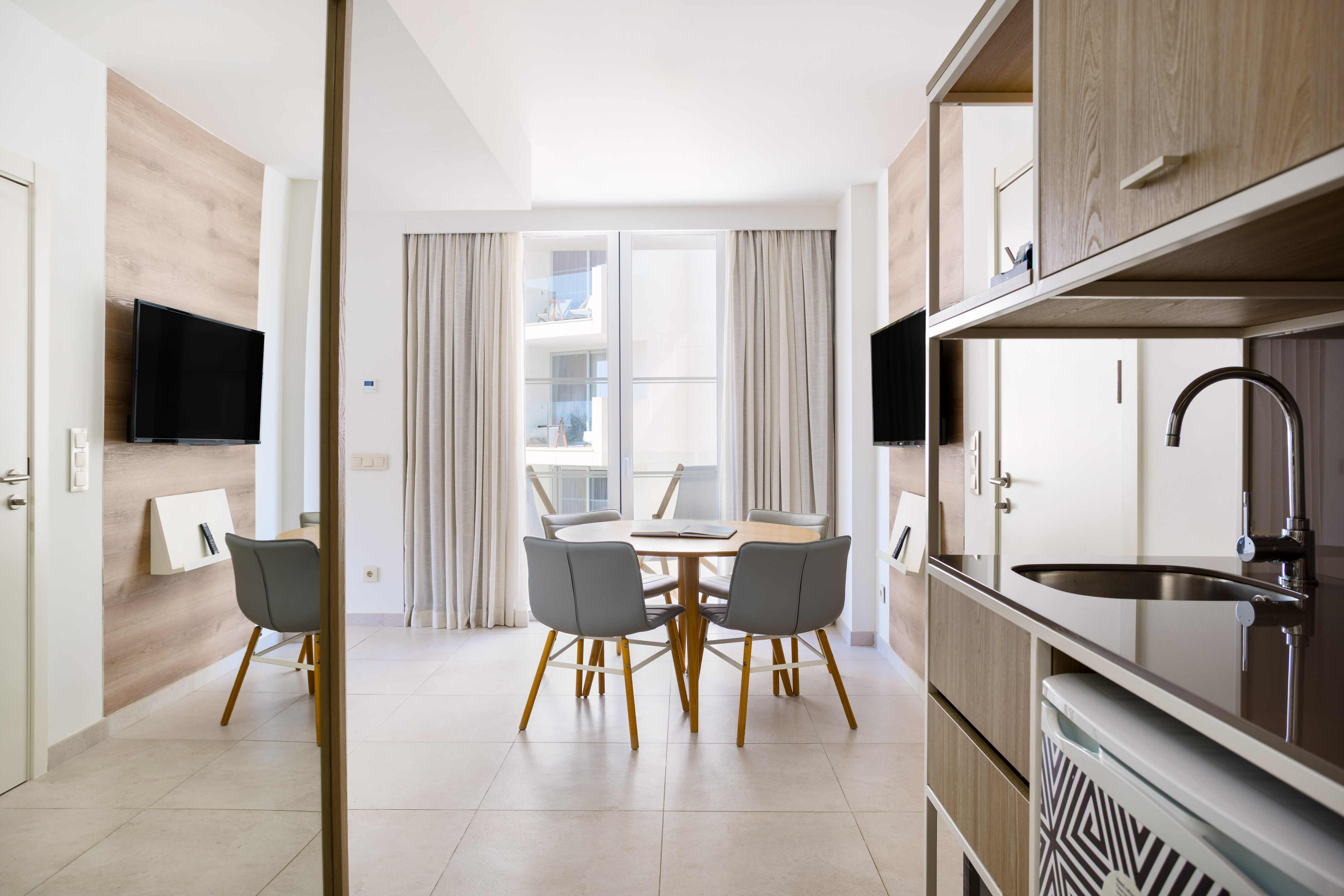Modern hotel apartment with dining table, TV, and compact kitchenette.