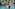 Woman in white bikini, gold necklace, swimming in resort pool with palm trees.