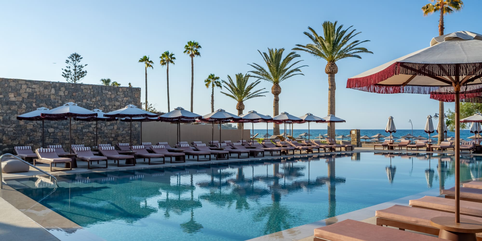 Luxury hotel pool with lounge chairs, palm trees, and ocean view resort.