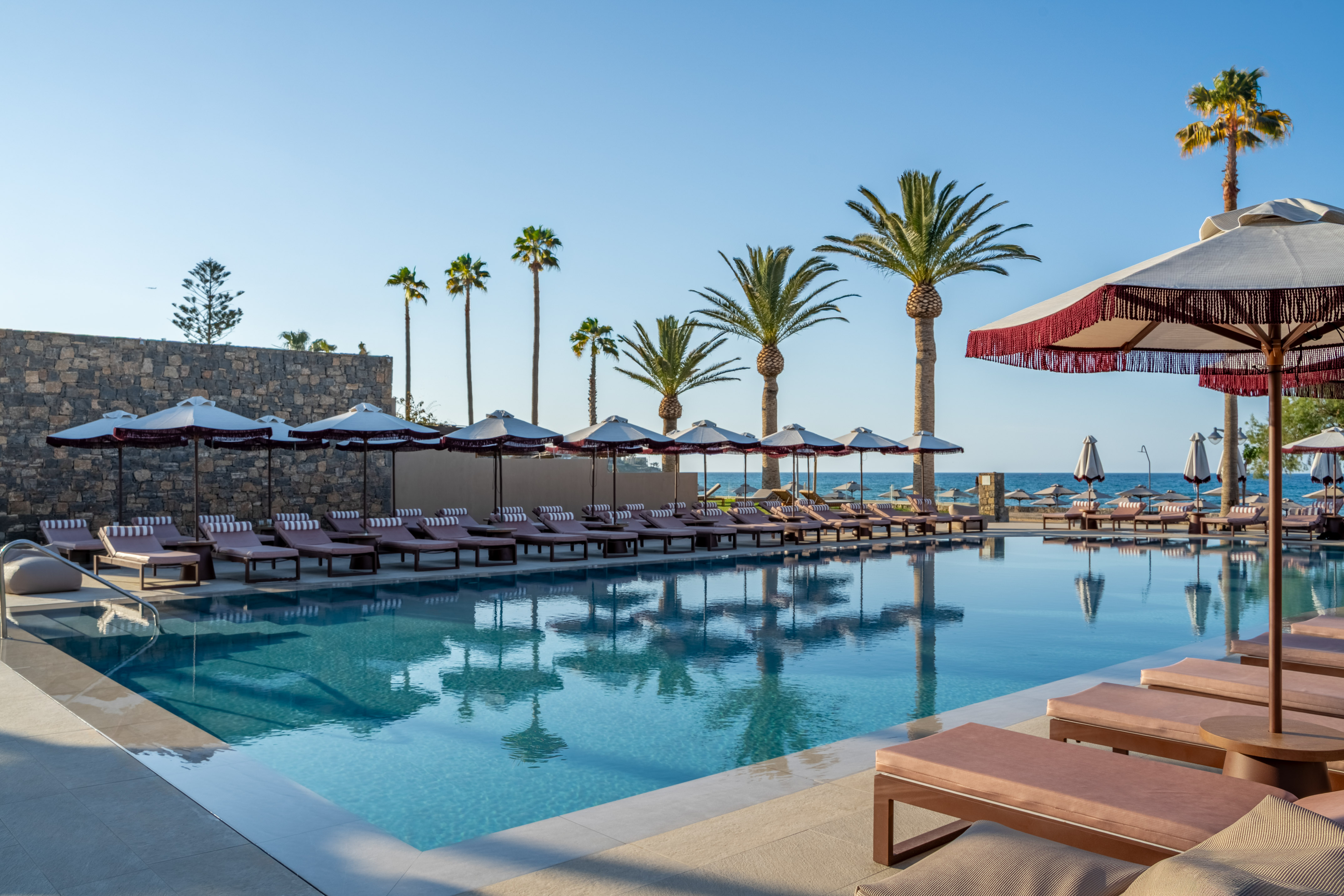 Luxury hotel pool with lounge chairs, palm trees, and ocean view resort.