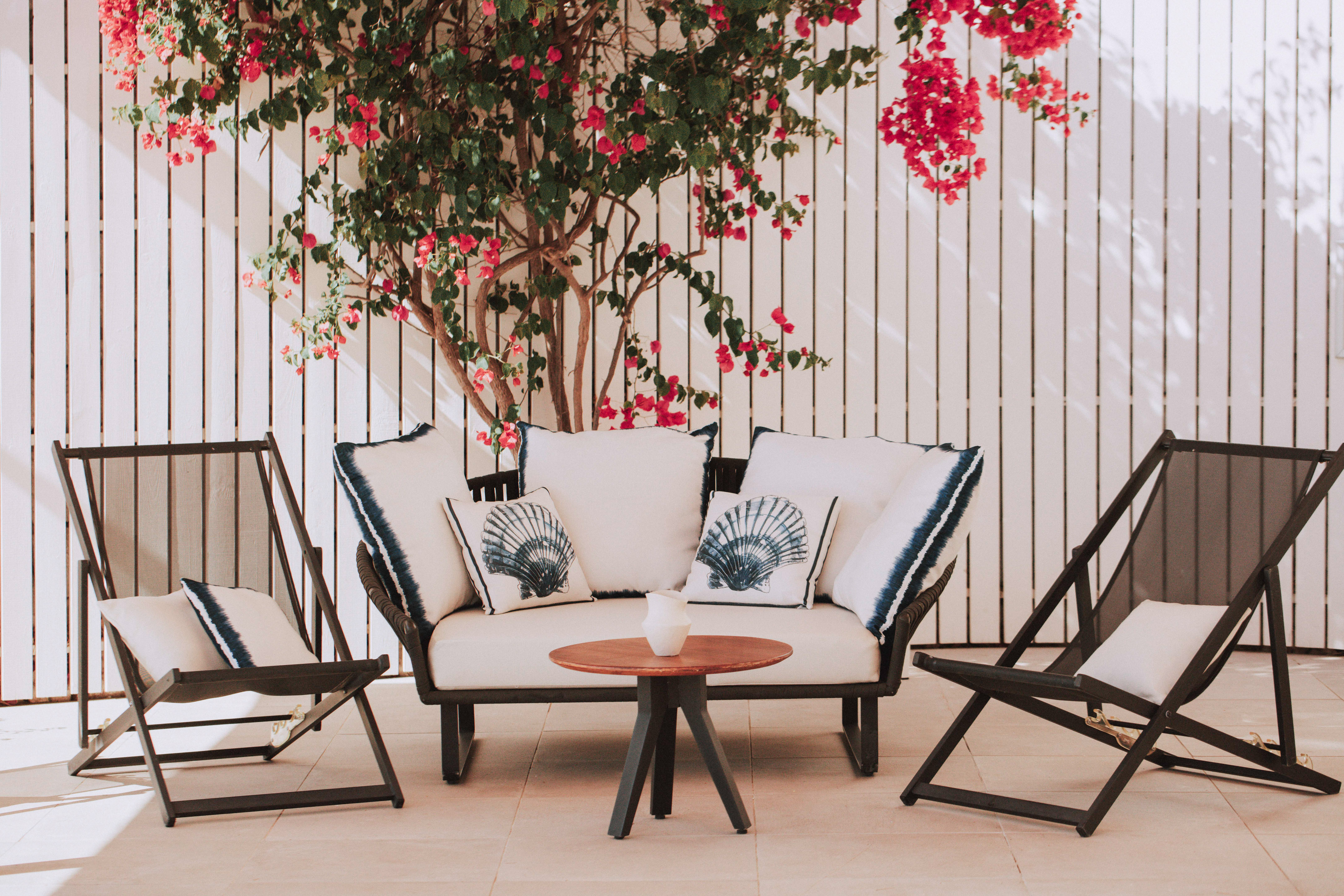 Outdoor patio lounge set with white sofa, chairs, and vibrant red bougainvillea.