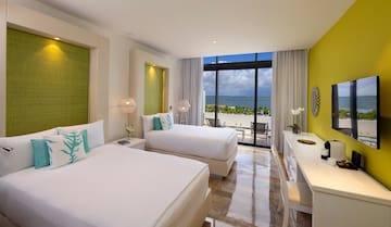 a room with two beds and a table with a view of the ocean