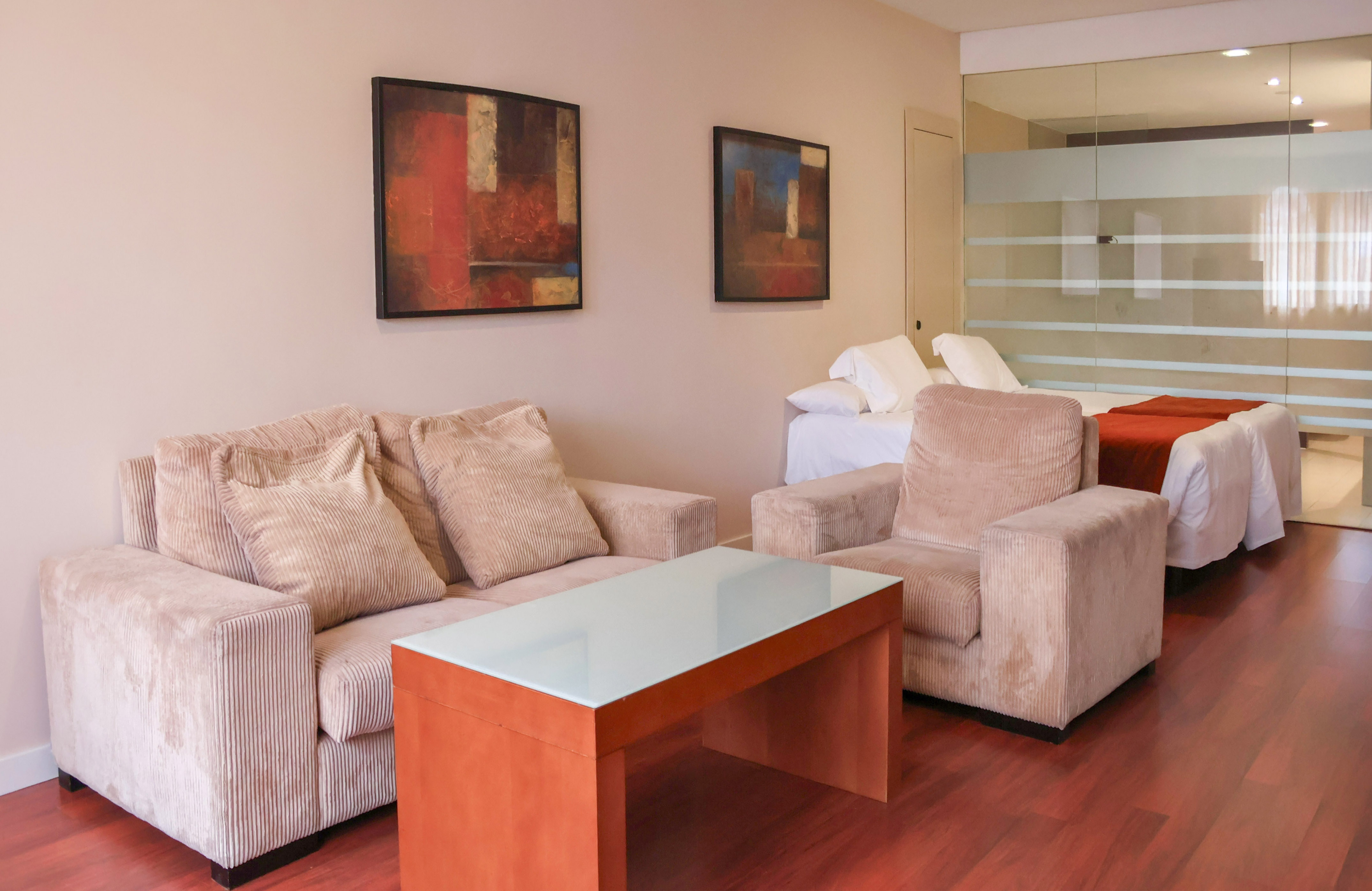Modern hotel suite with living area, two beds, abstract art, and glass partition.