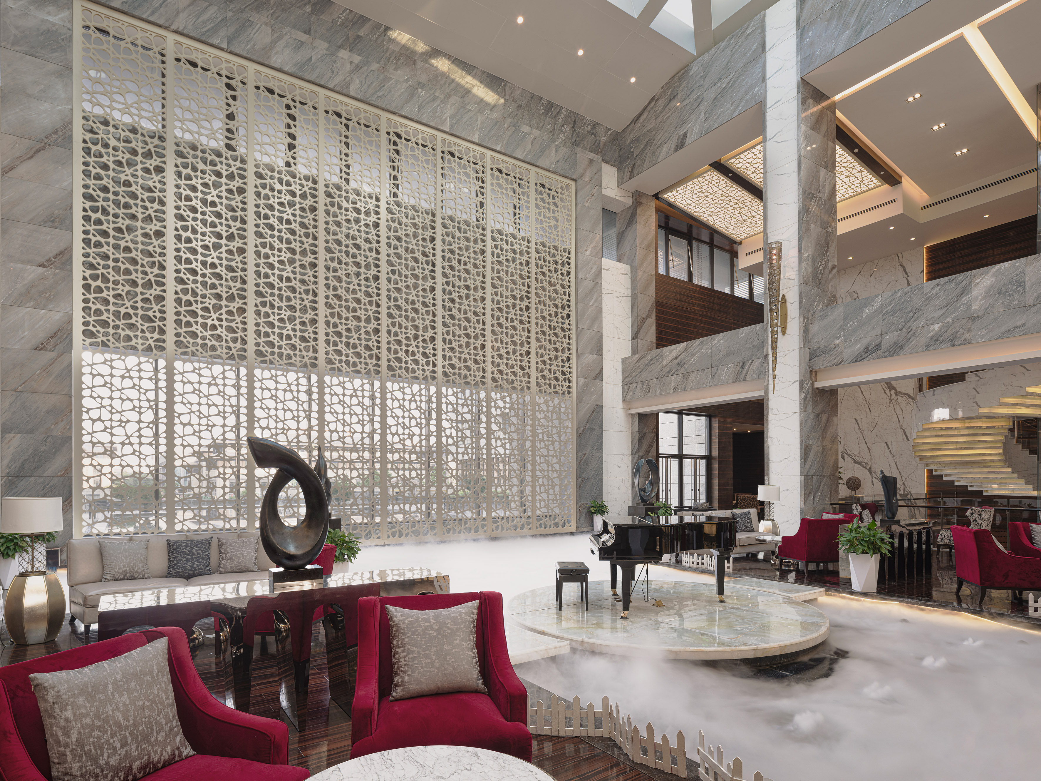 Luxury hotel lobby with grand piano, red seating, marble walls, and decorative screen.