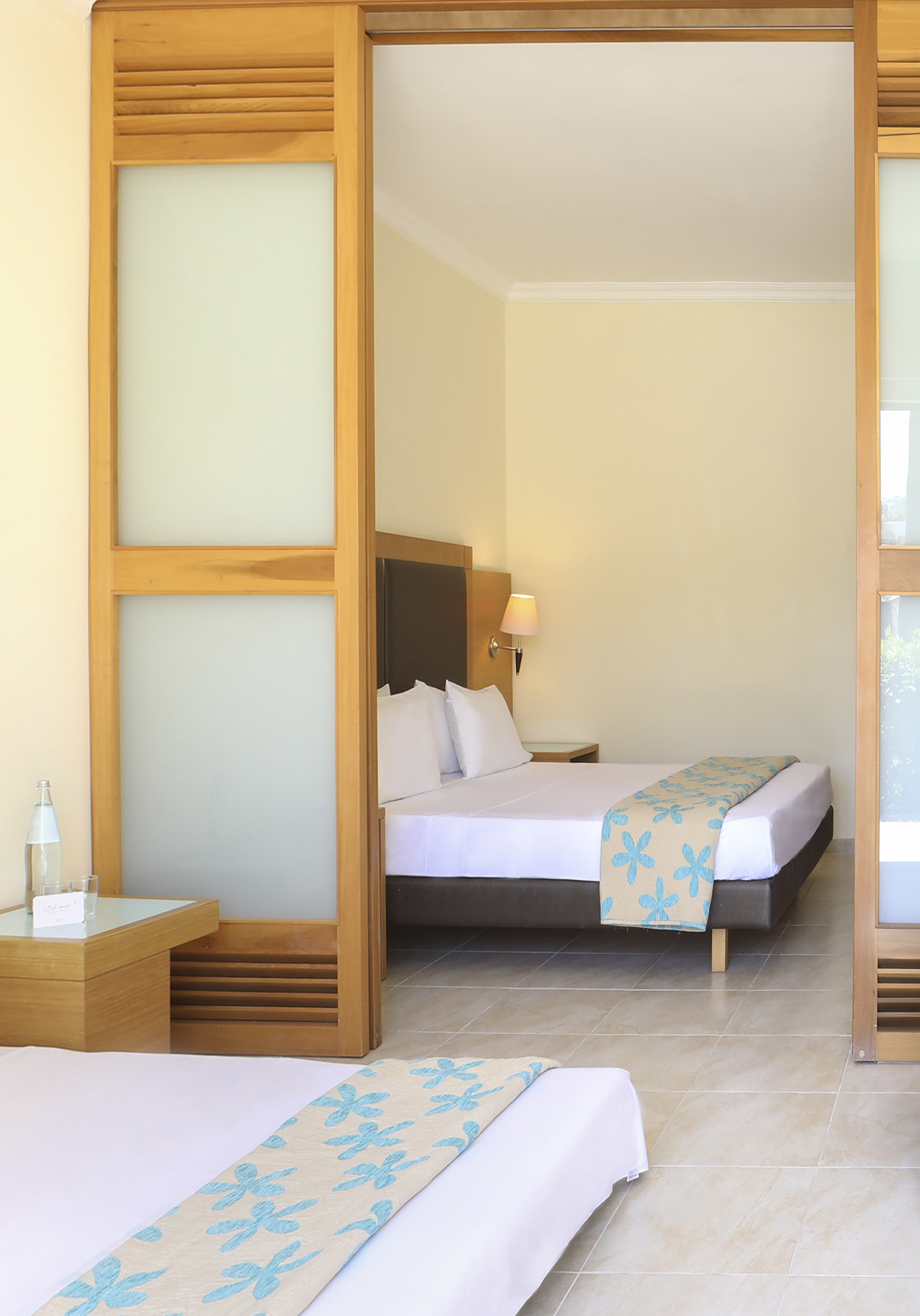 Modern hotel room interior with two beds, wooden sliding doors, and blue floral decor.