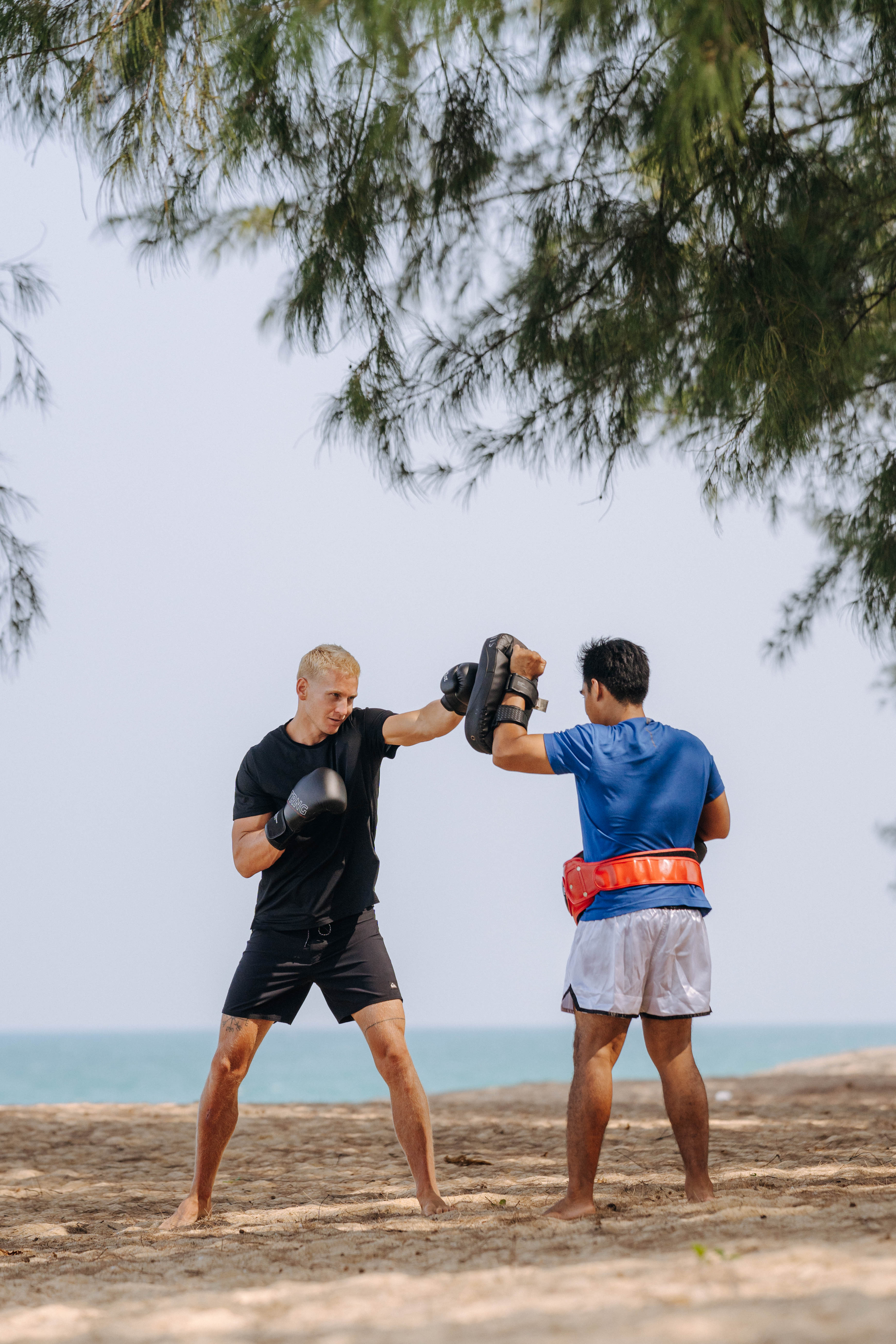 Blond boxer punching pads with a trainer during a beach workout.