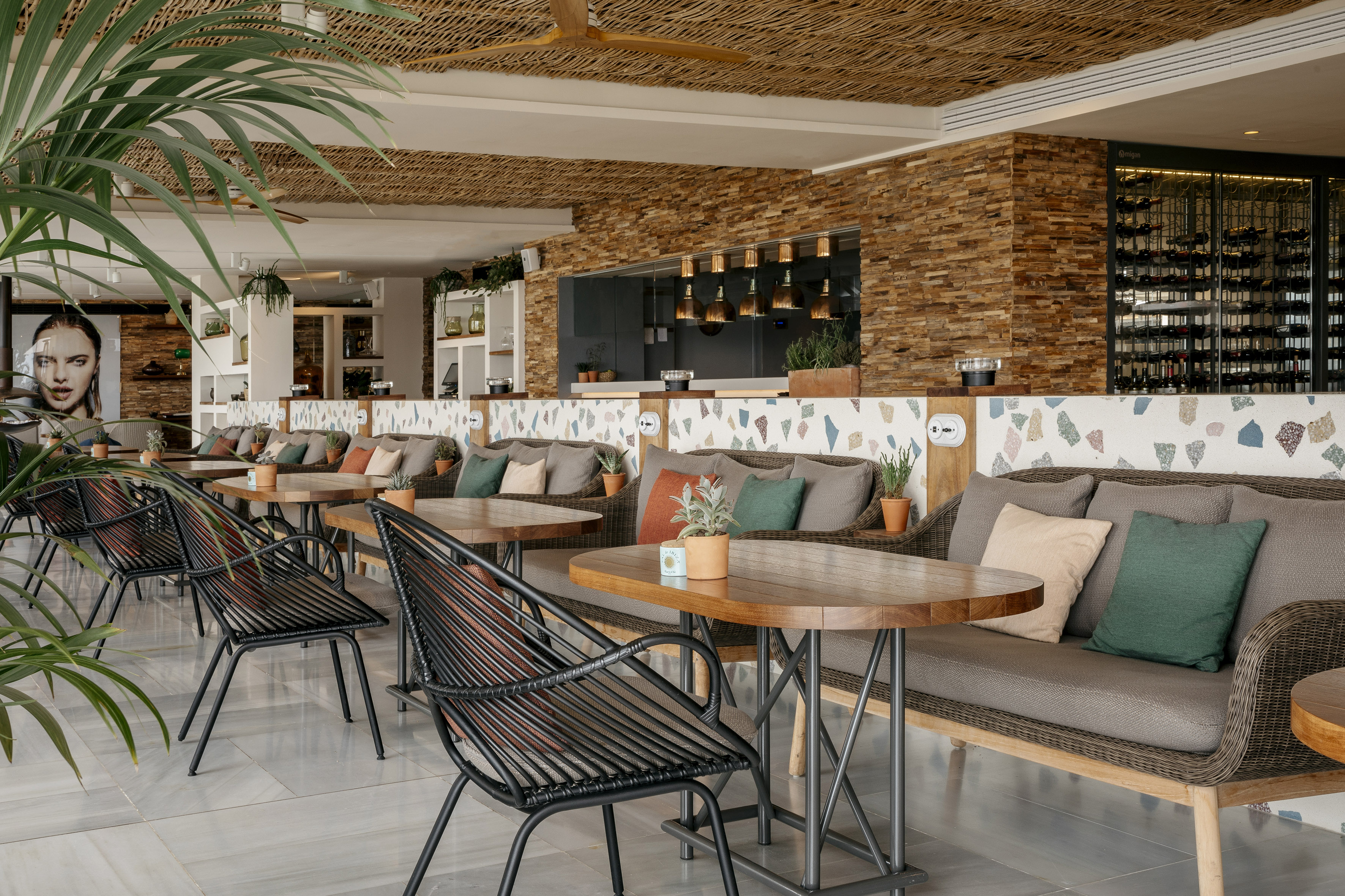Modern cafe interior with rattan sofas, wooden tables, and lush plants.