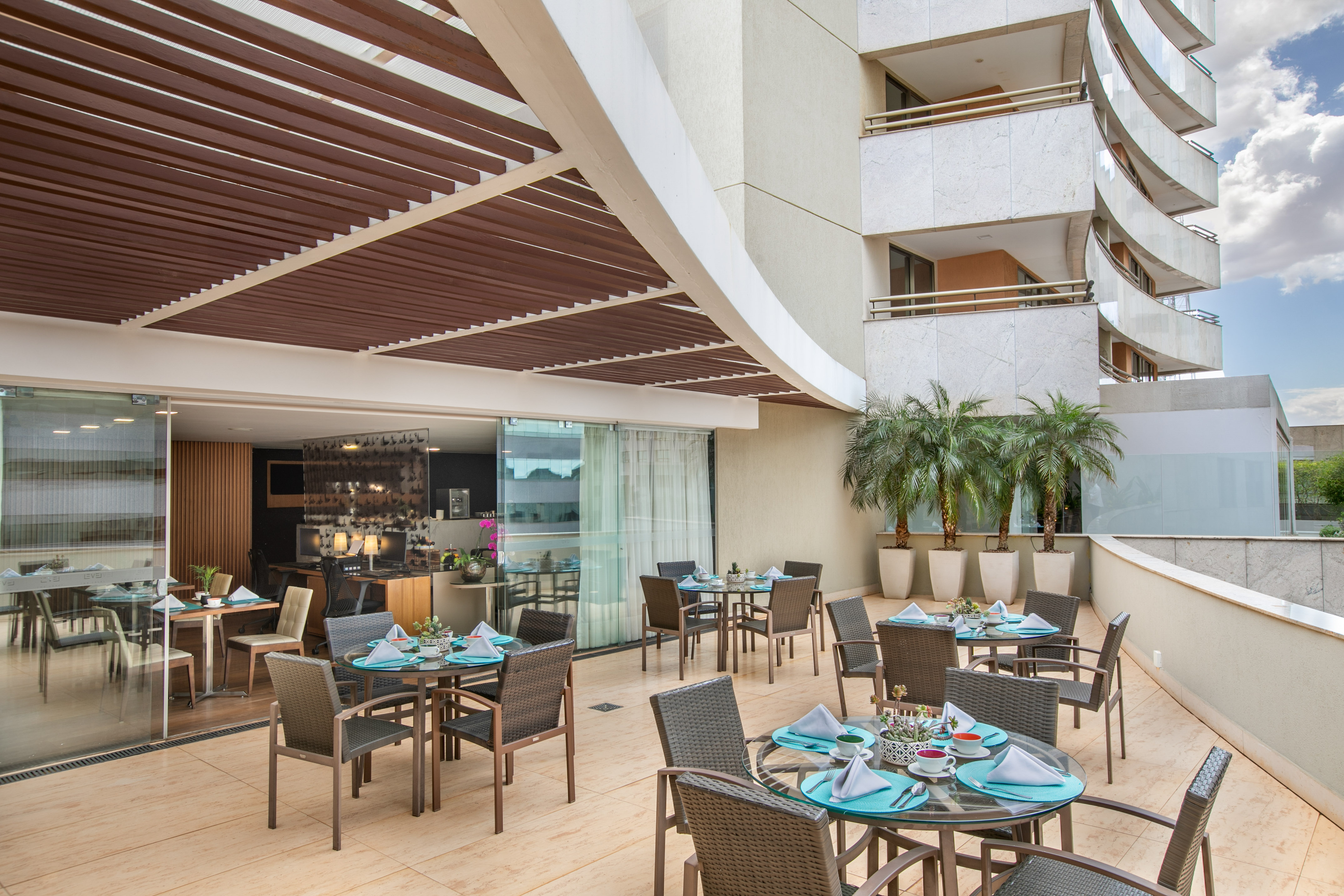 Modern outdoor dining terrace with set tables, chairs, and palm trees.
