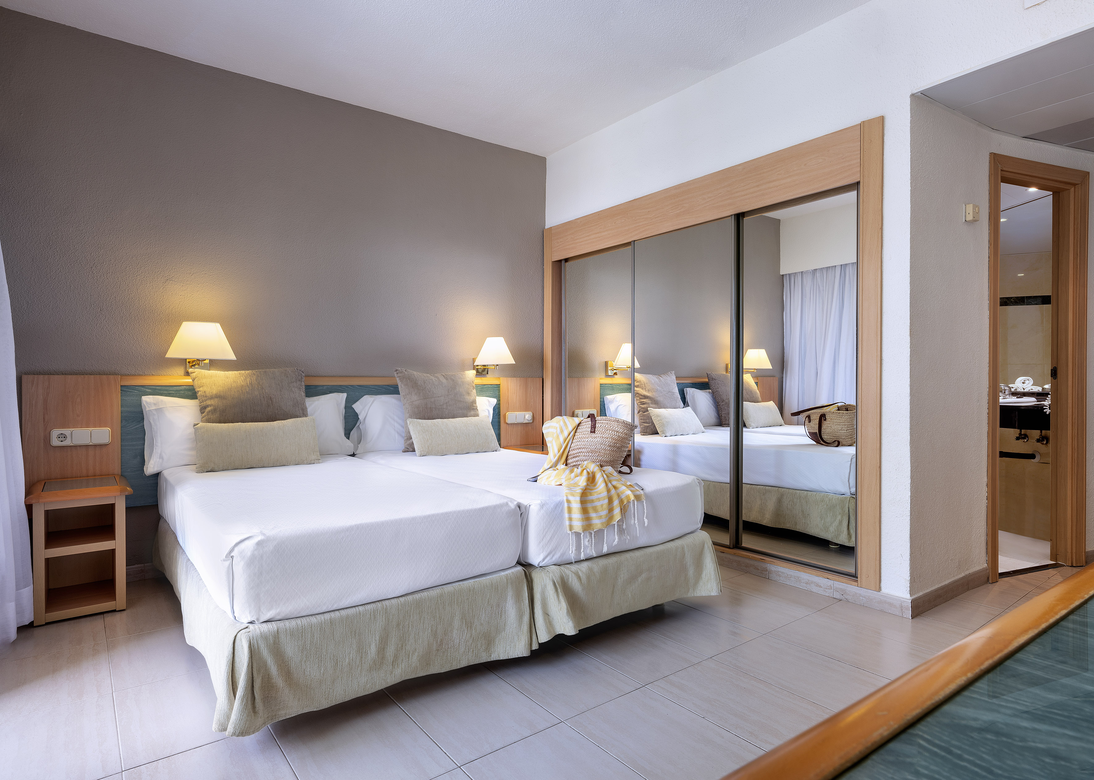 Hotel room with two single beds, bedside lamps, and mirrored wardrobe.
