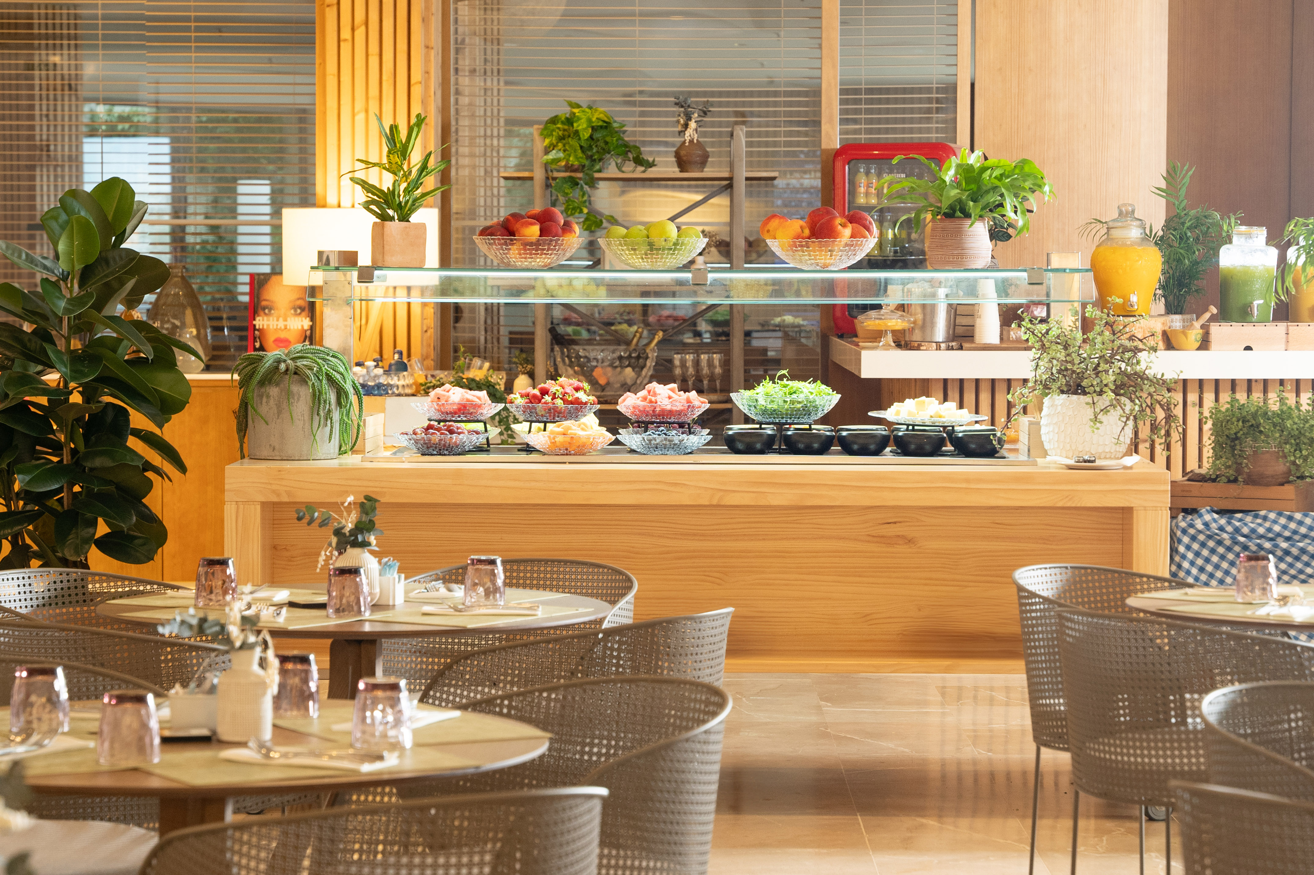 Bright hotel restaurant buffet with fresh fruits, salads, and juices.