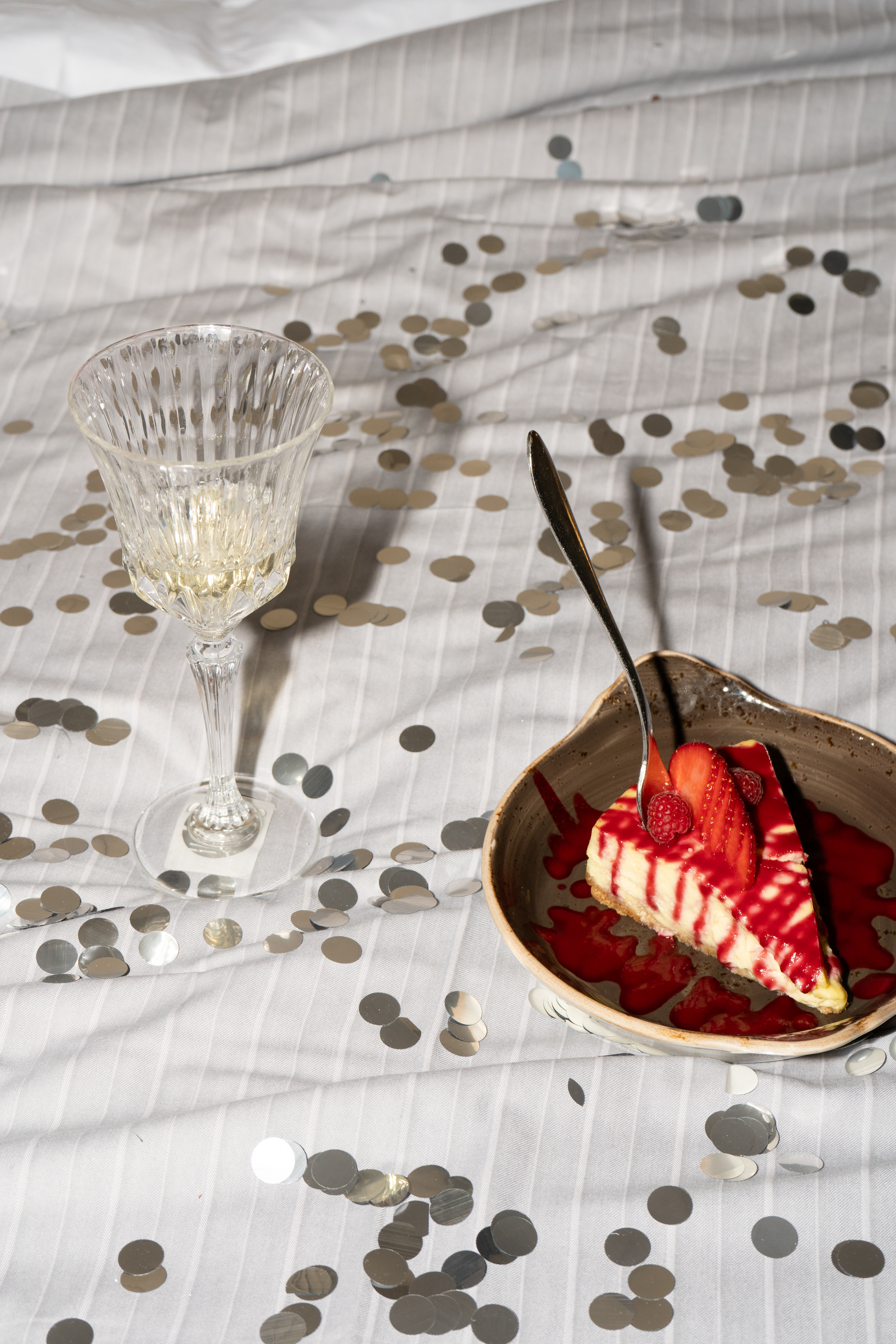 Strawberry raspberry cheesecake with red sauce, wine, and silver confetti.