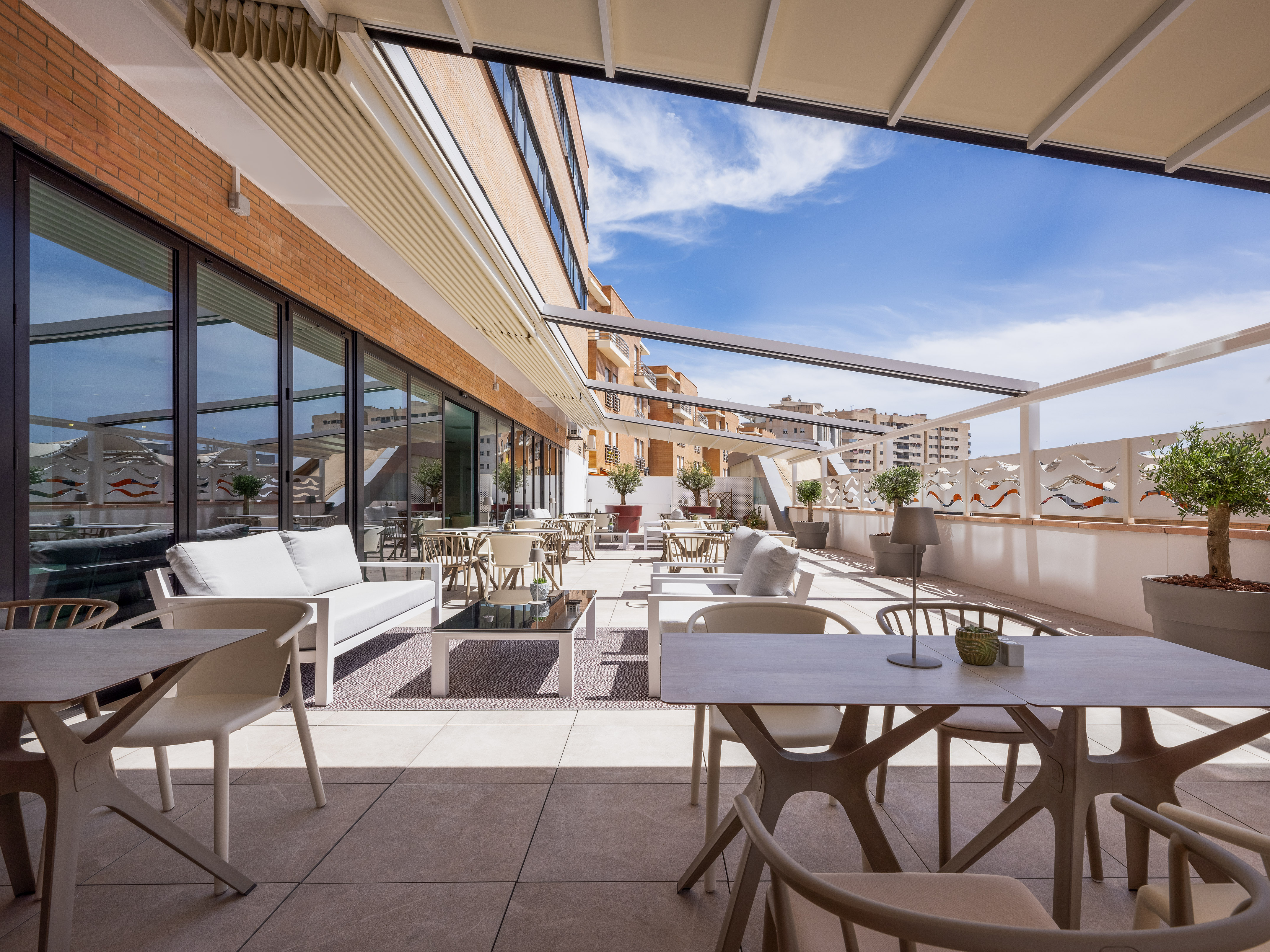 Modern hotel terrace, retractable awning, outdoor dining furniture.