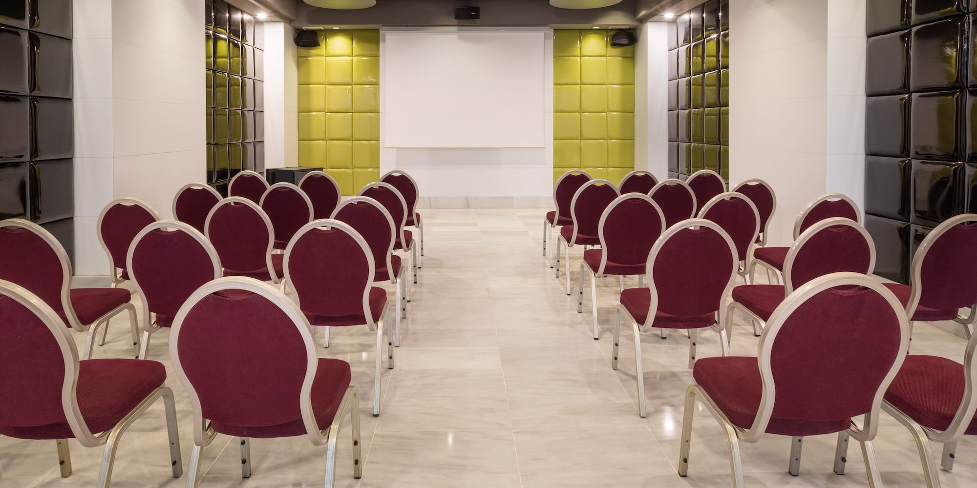 Modern conference room with burgundy chairs, white screen, and green/black quilted walls.