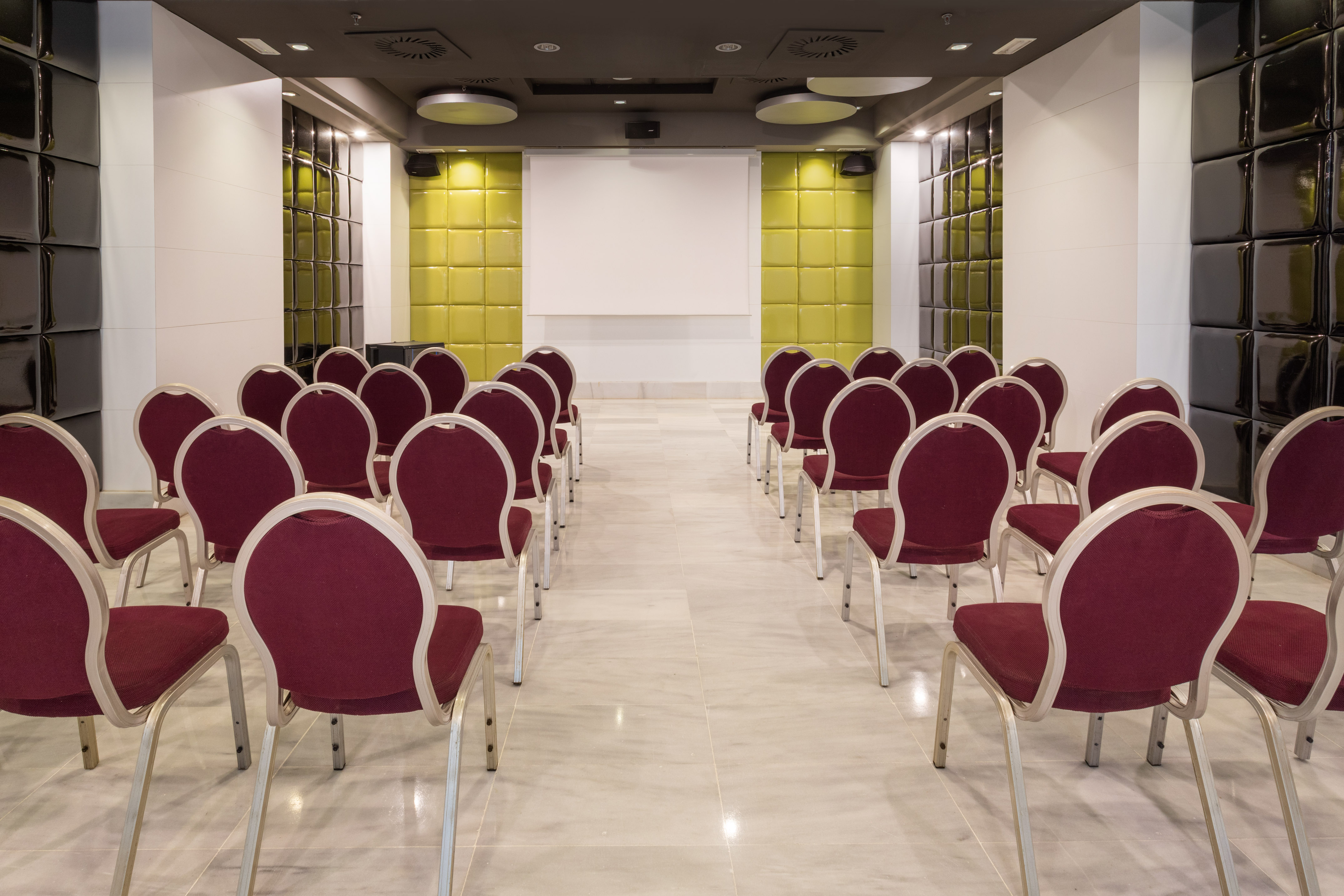 Modern conference room with burgundy chairs, white screen, and green/black quilted walls.