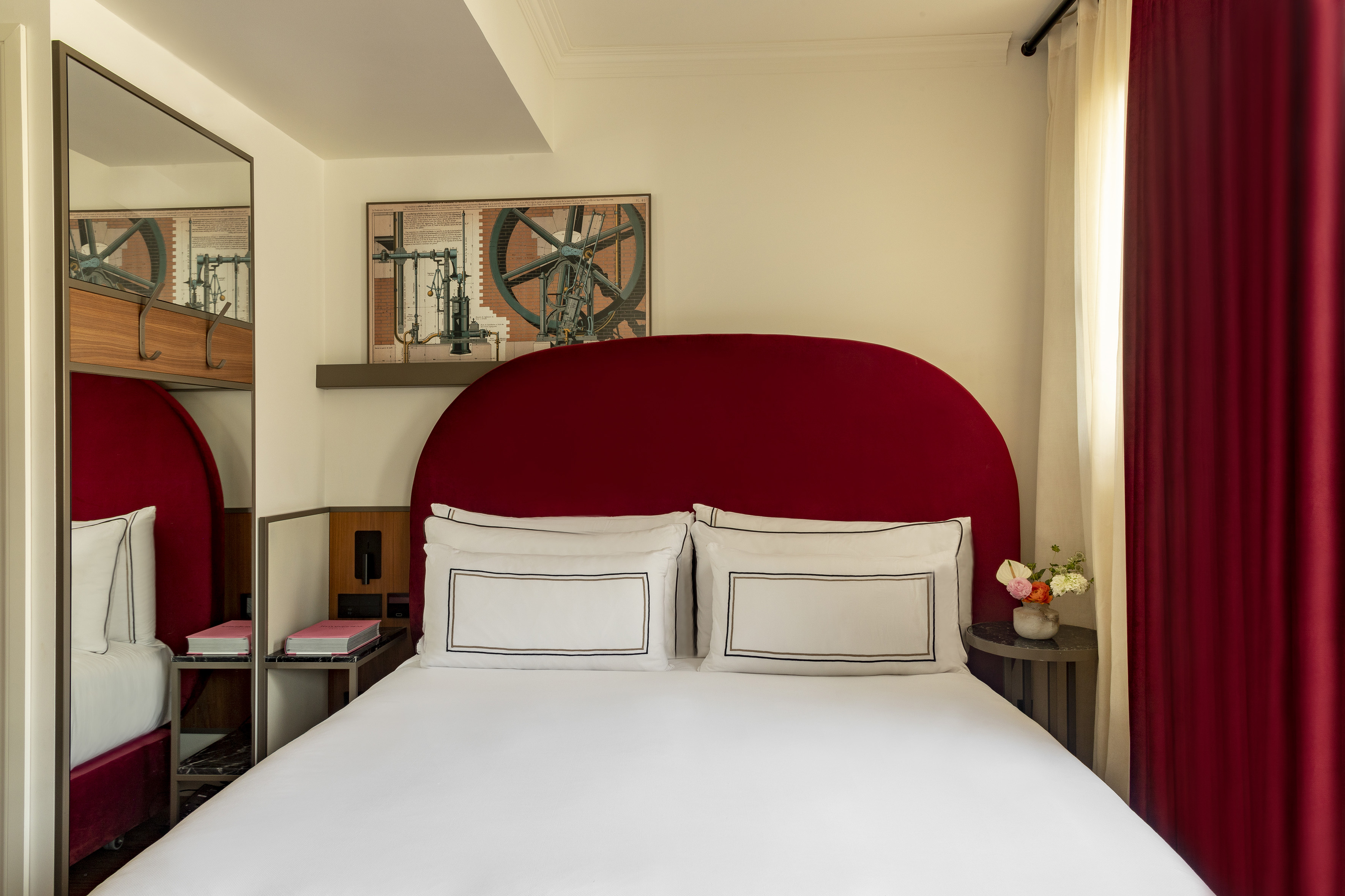 Modern hotel bedroom with red curved headboard, white bed, and industrial art.