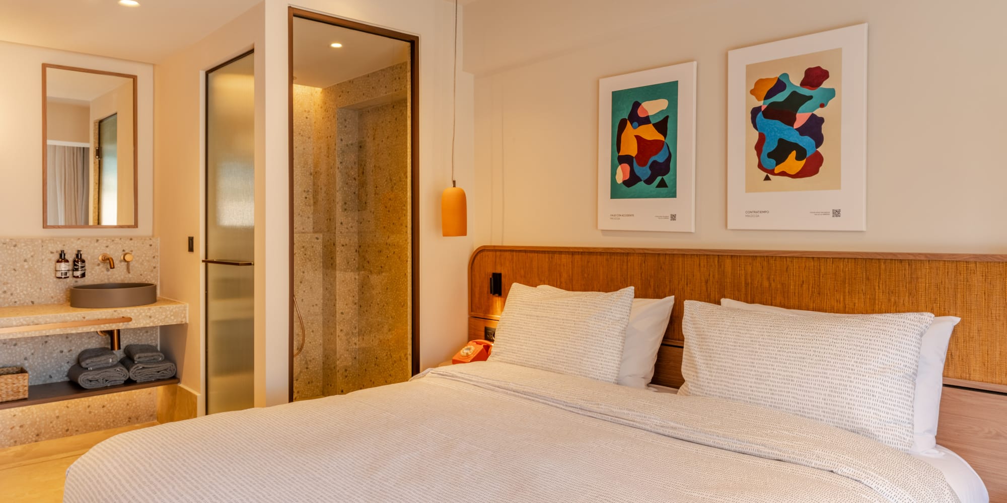 a bed with white sheets and pillows in a room with art on the wall