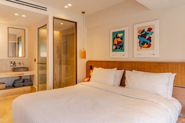 a bed with white sheets and pillows in a room with art on the wall