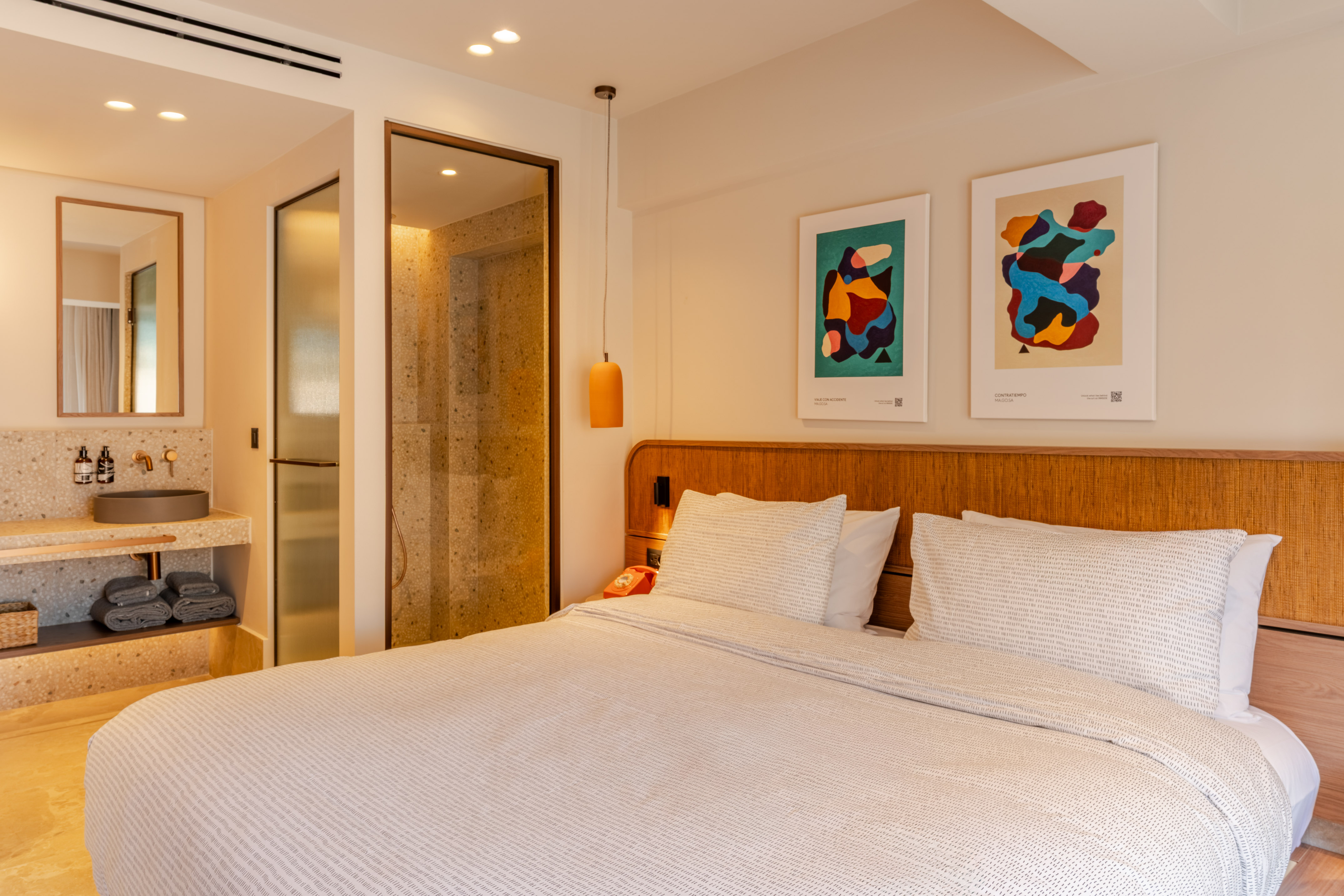 Modern hotel room with bed, abstract art, and terrazzo bathroom.