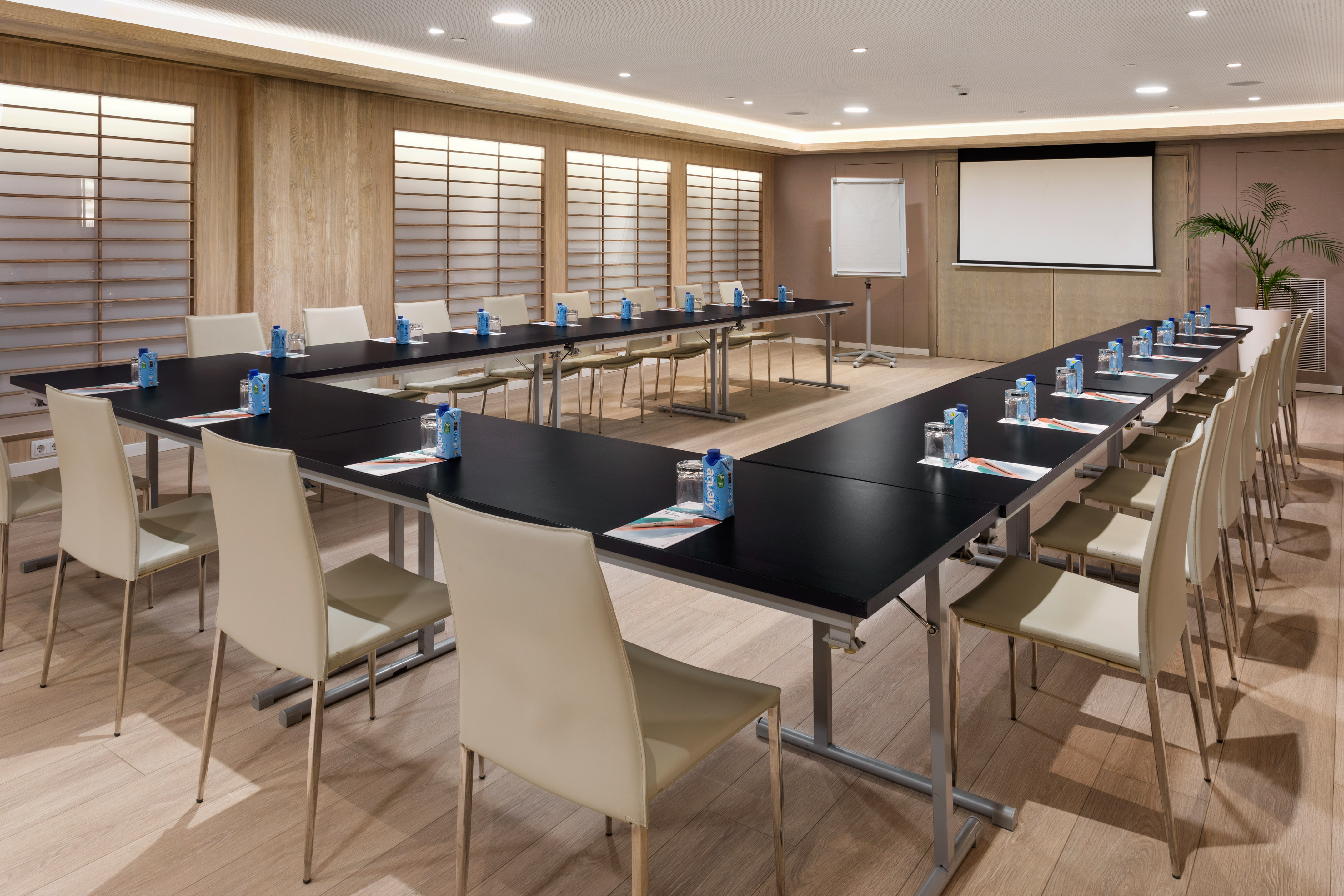 Modern conference room with U-shaped table, projector screen, and whiteboard.