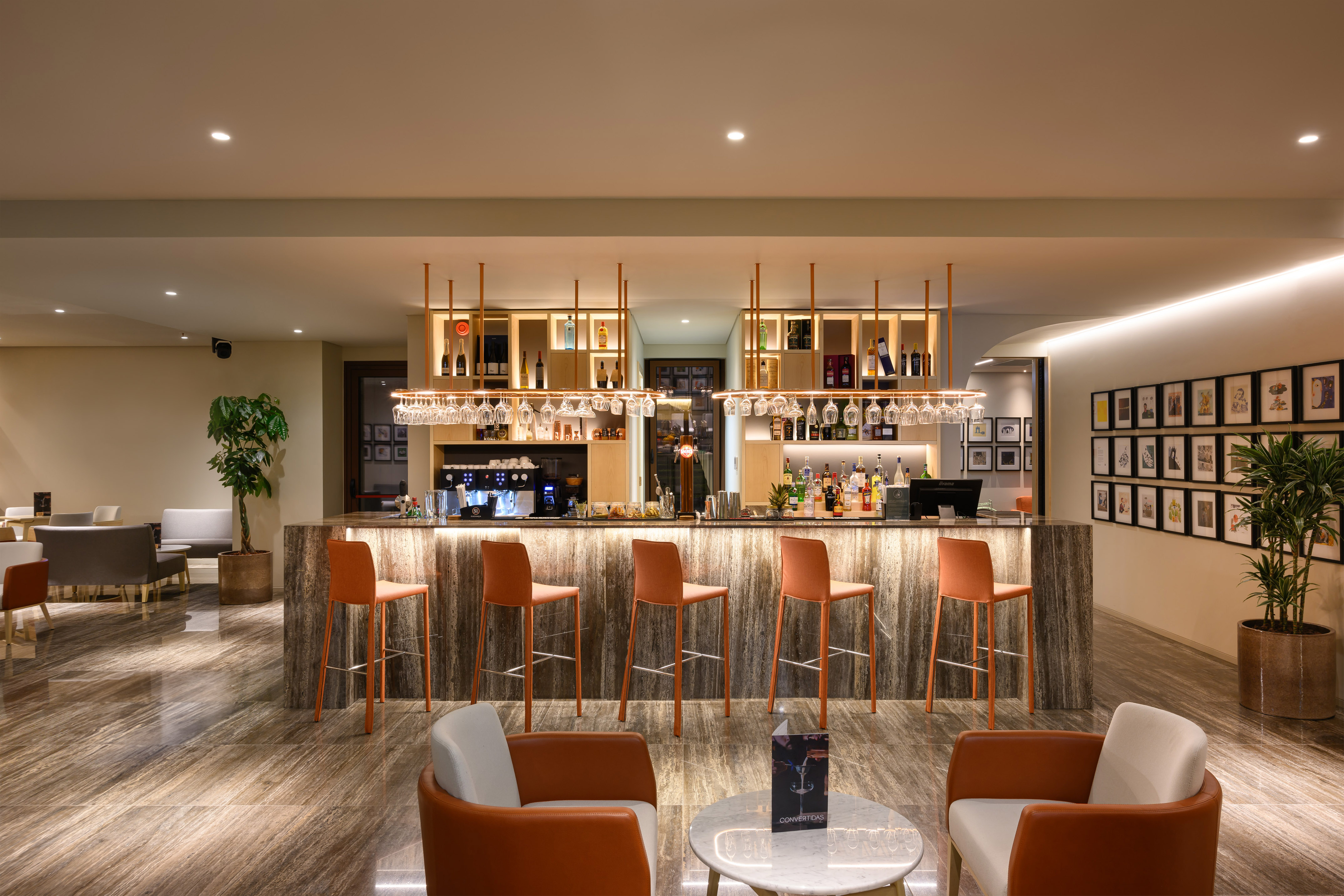 Modern hotel bar with marble counter, orange barstools, and hanging wine glasses. - INNSiDE Braga Centro, Braga