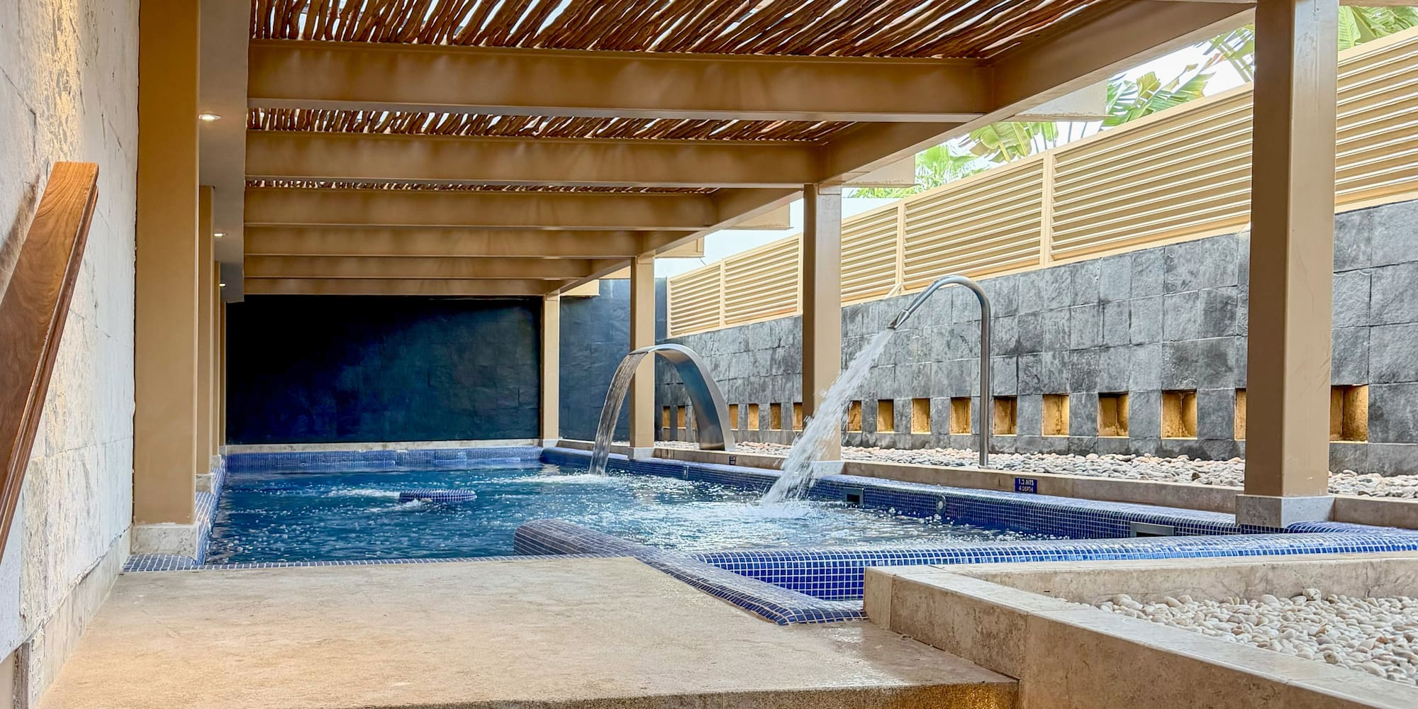 Modern spa with hydrotherapy pool, wooden pergola roof, and lighted steps.
