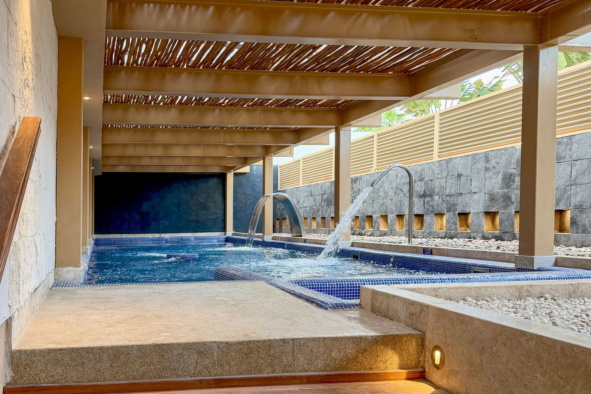 Modern spa with hydrotherapy pool, wooden pergola roof, and lighted steps.