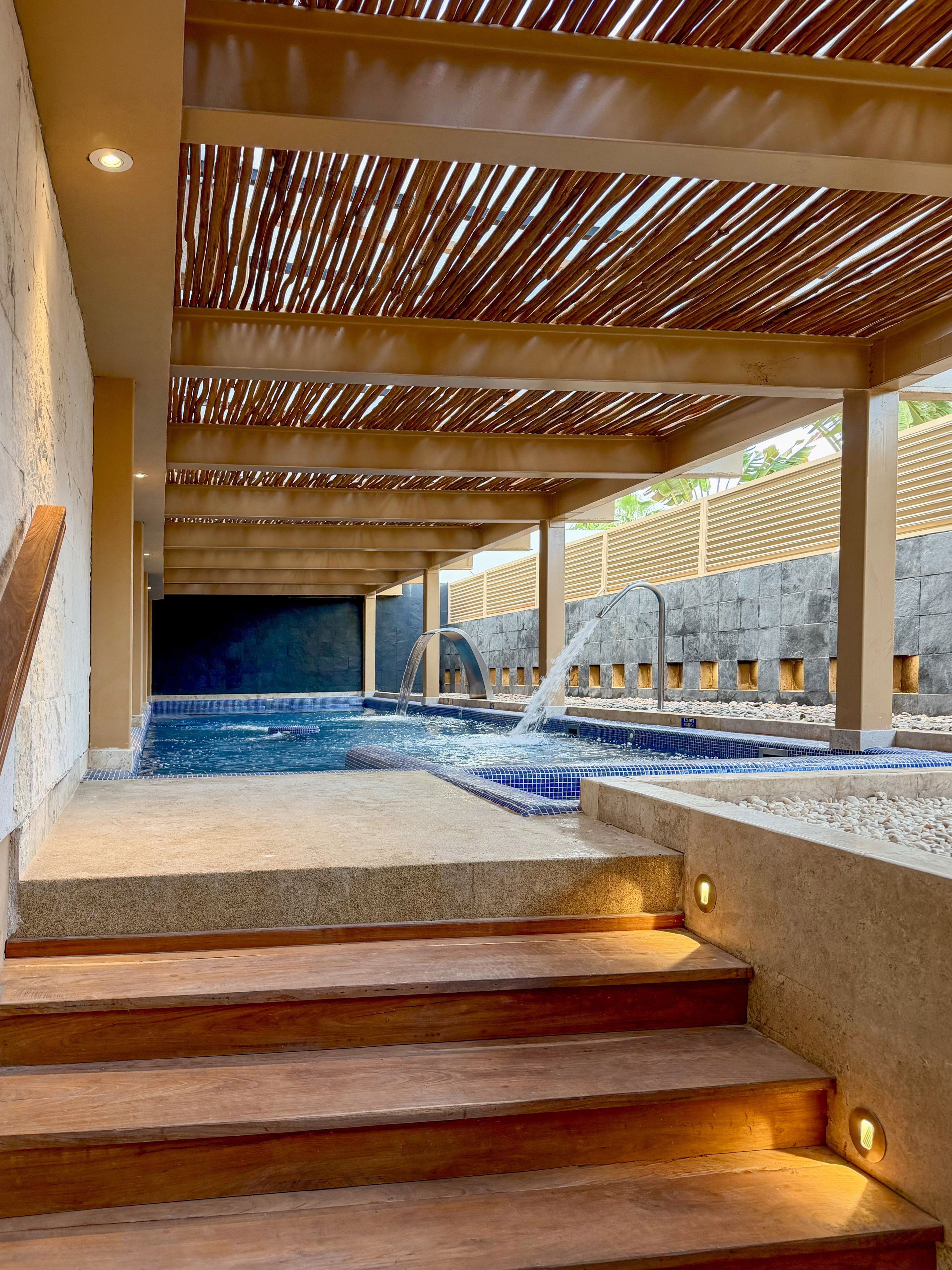 Modern spa with hydrotherapy pool, wooden pergola roof, and lighted steps.
