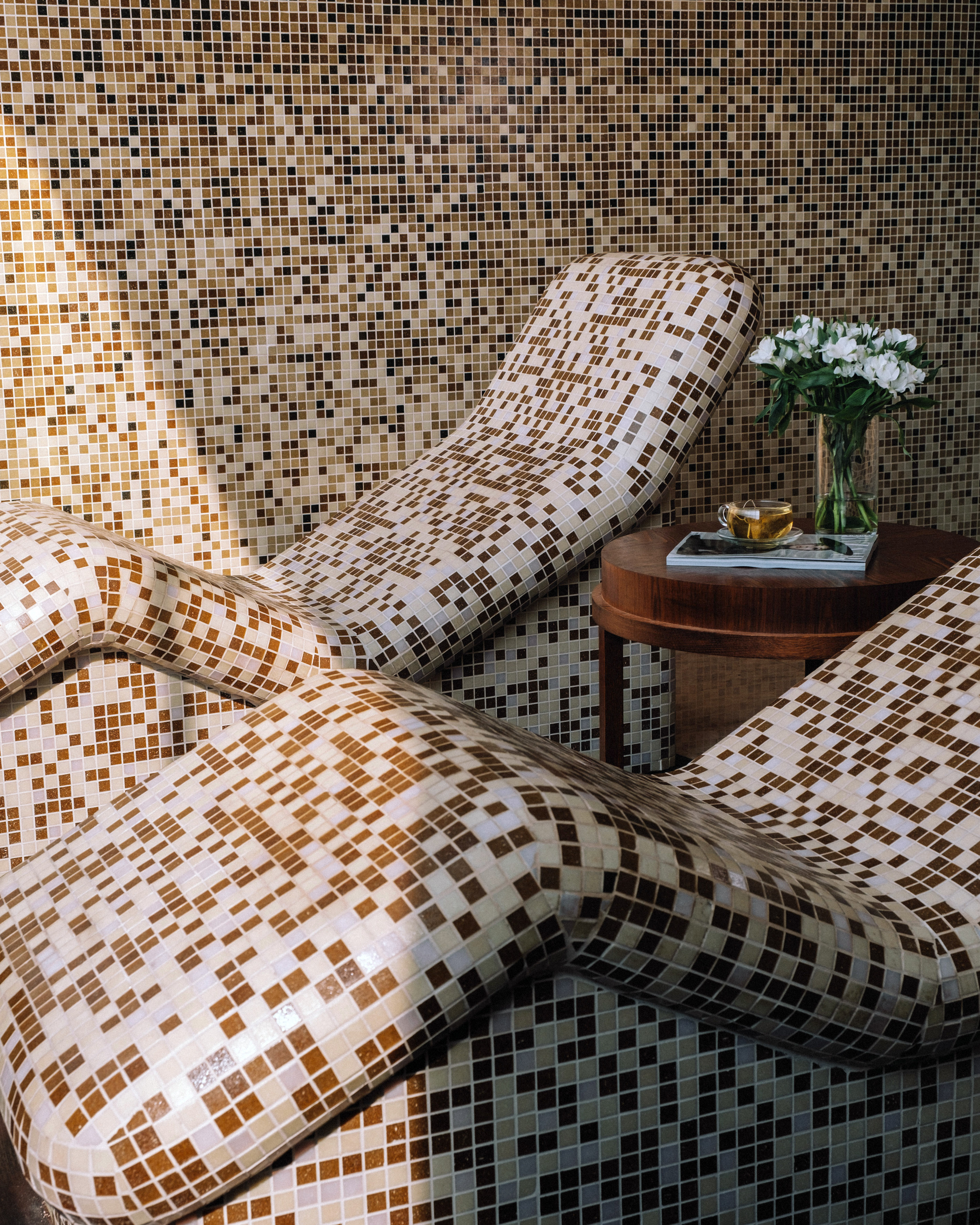 Heated mosaic tiled spa loungers with tea and flowers, promoting relaxation.